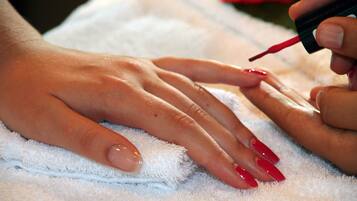A close-up of hands with red nail polish being applied.