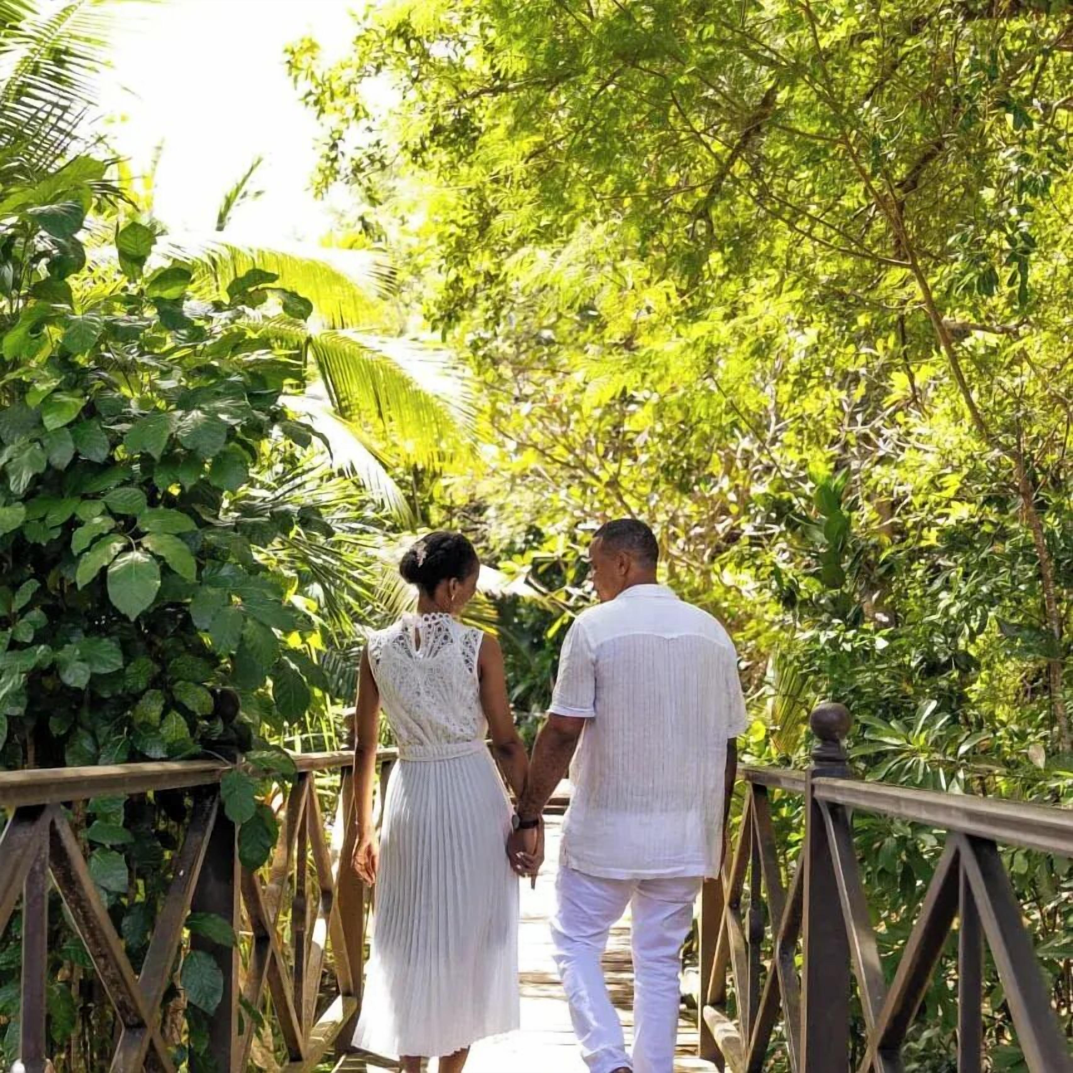 A couple walking on a wooden bridge surrounded by lush greenery.
