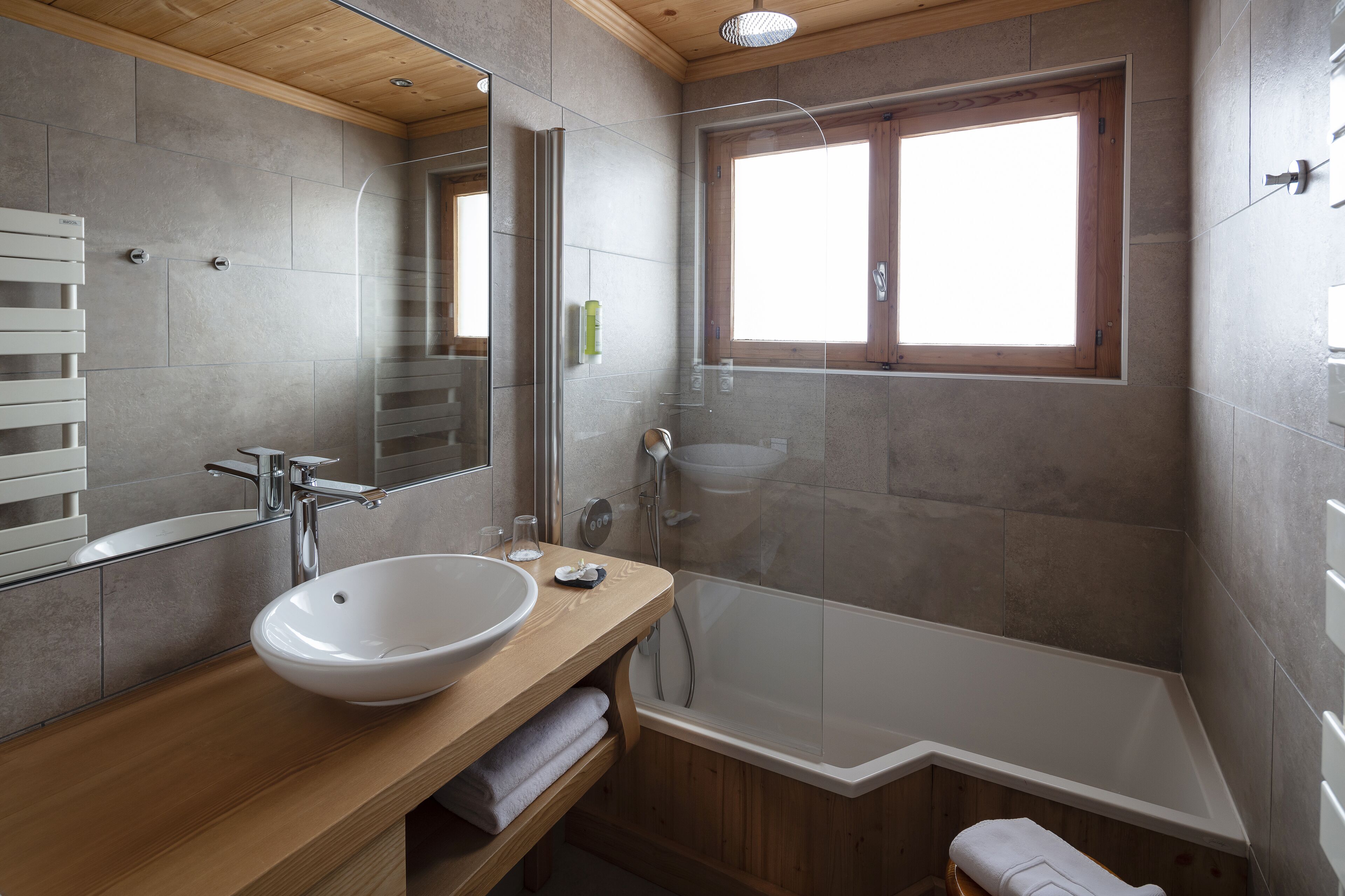 A modern bathroom with a large white sink, a glass-enclosed shower, and a wooden vanity.