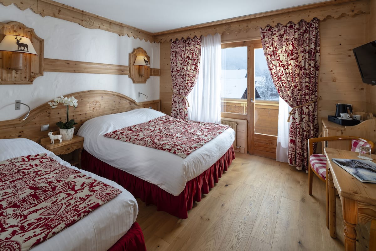 A wooden cabin room with two beds, a wooden table, a chair, a TV, and a window with curtains.