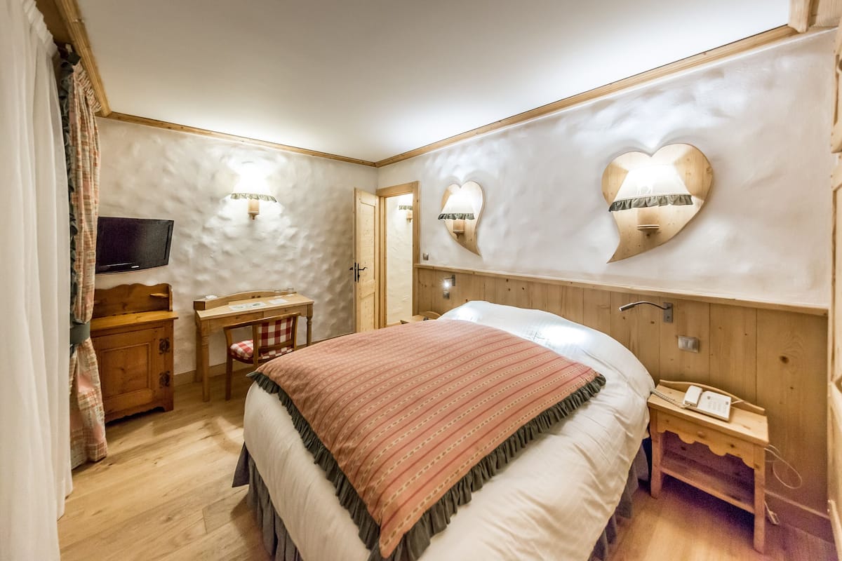 A bedroom with a bed, a desk, a chair, a TV, and two wall-mounted light fixtures.
