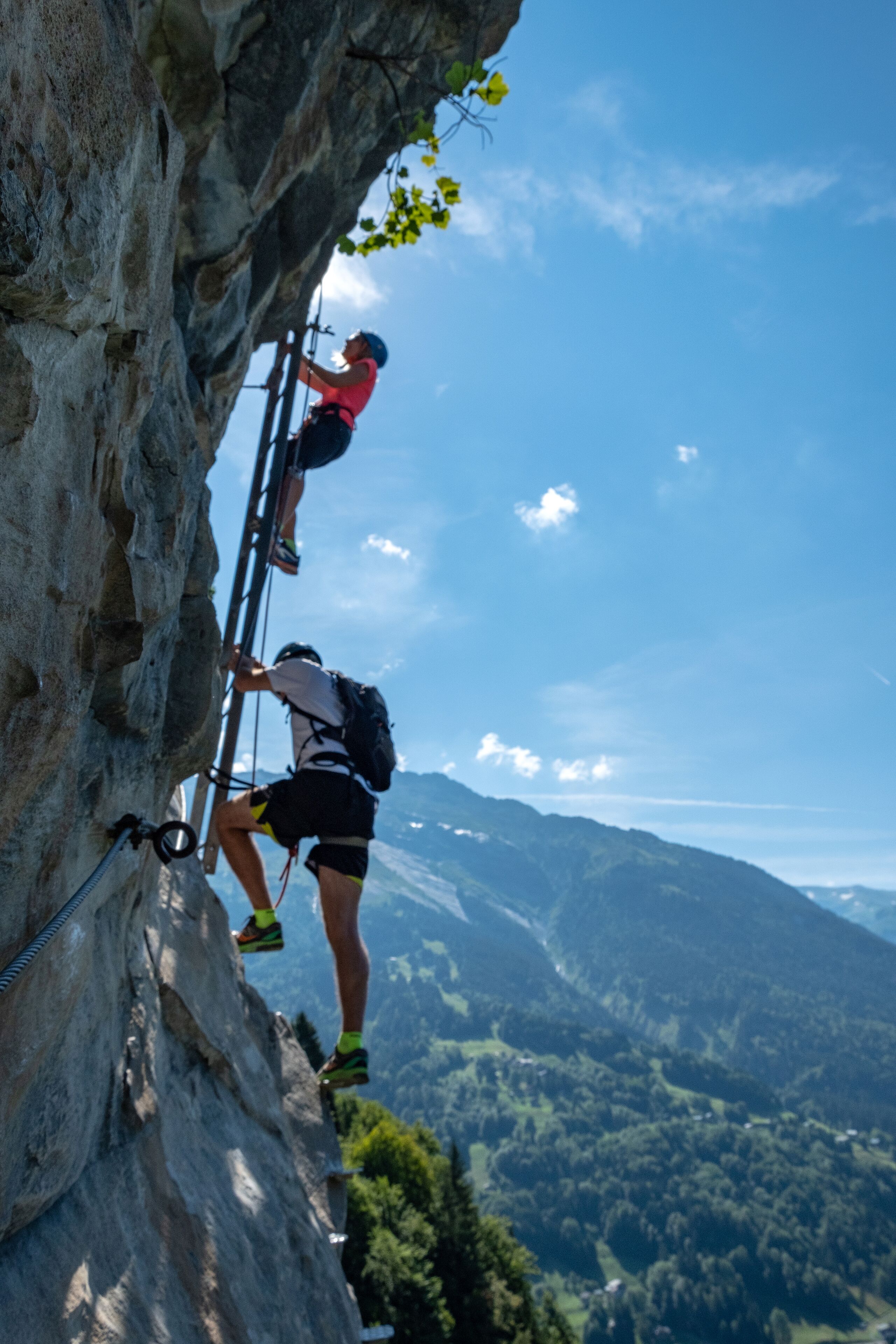 Una persona escalando una pared rocosa con una vista despejada de un paisaje montañoso al fondo.
