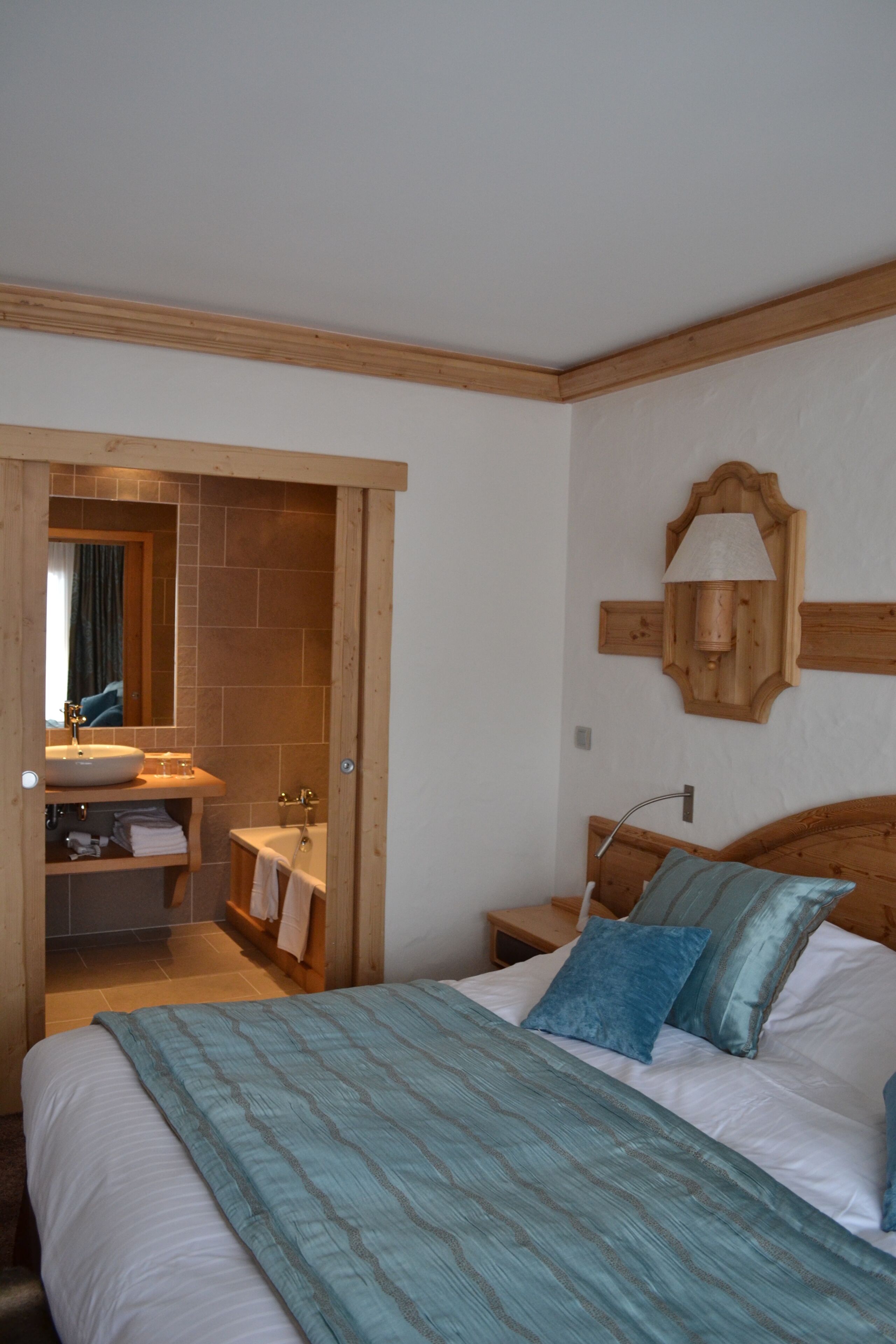 A bedroom with a bed, a wooden headboard, a nightstand, a bedside table, a mirror, and a bathroom visible through an open door.