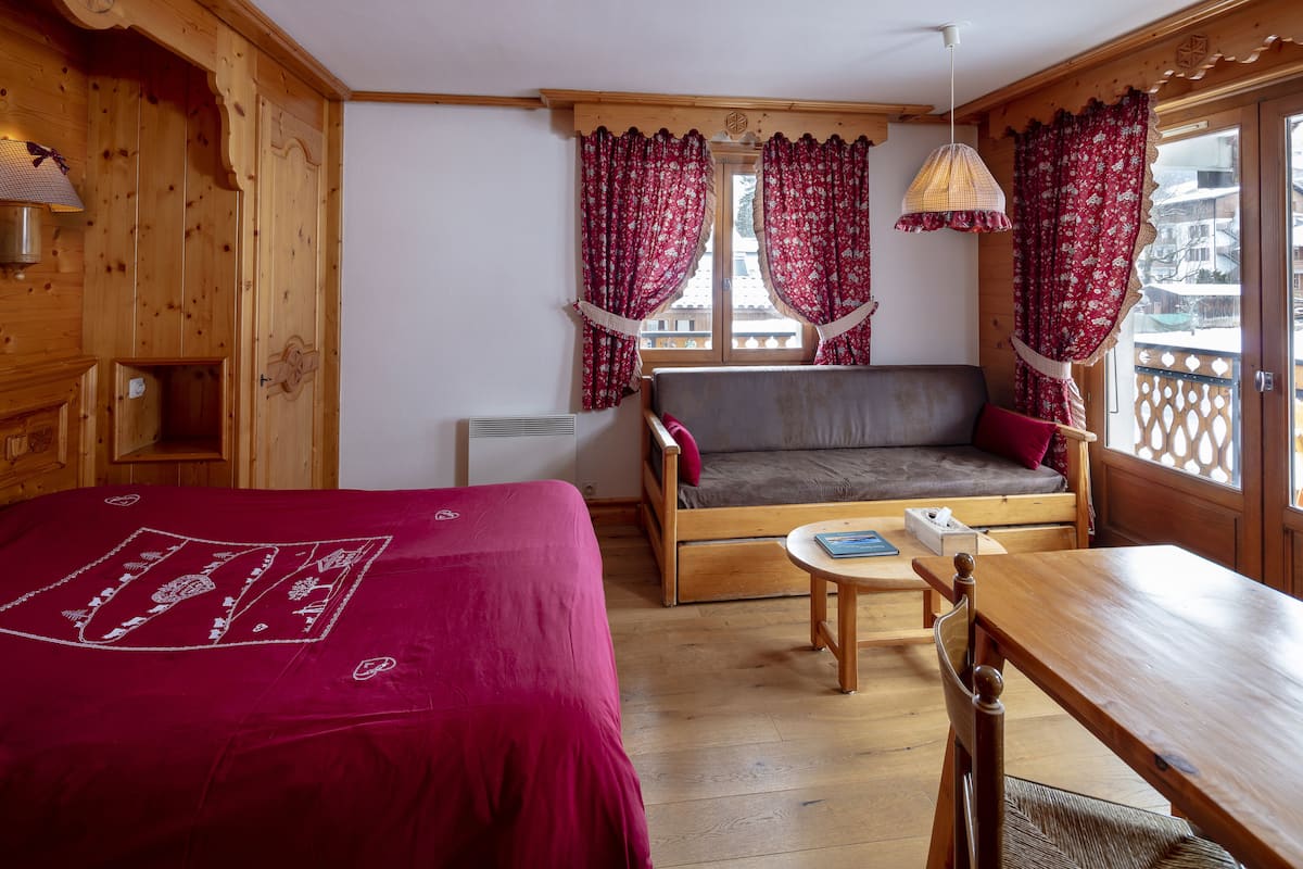 A wooden room with a bed, a sofa, a table, and curtains.