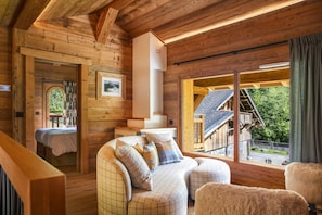 A wooden cabin interior with a sofa, a fireplace, and a view of a mountain. - Neige et Roc, The Originals Relais (Samoëns)