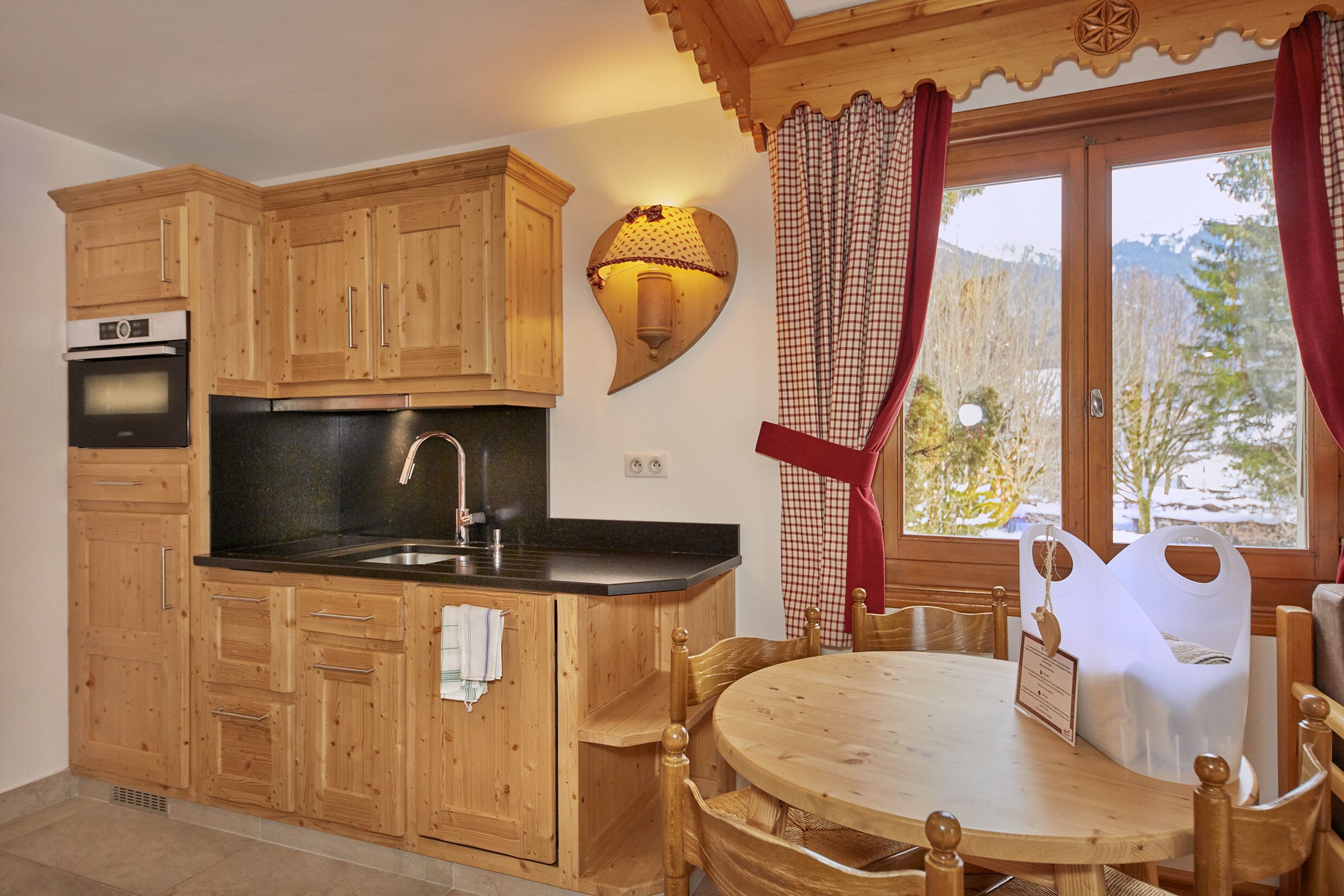 Een houten keuken met een zwart aanrecht, houten kastjes, een spoelbak en een eethoek met een ronde tafel en stoelen.