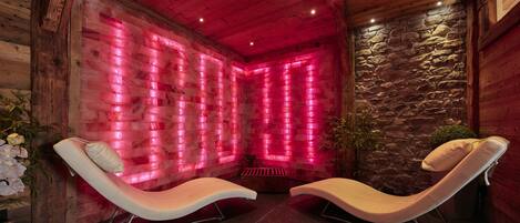 A spa room with wooden walls, stone accents, and two reclining chairs.