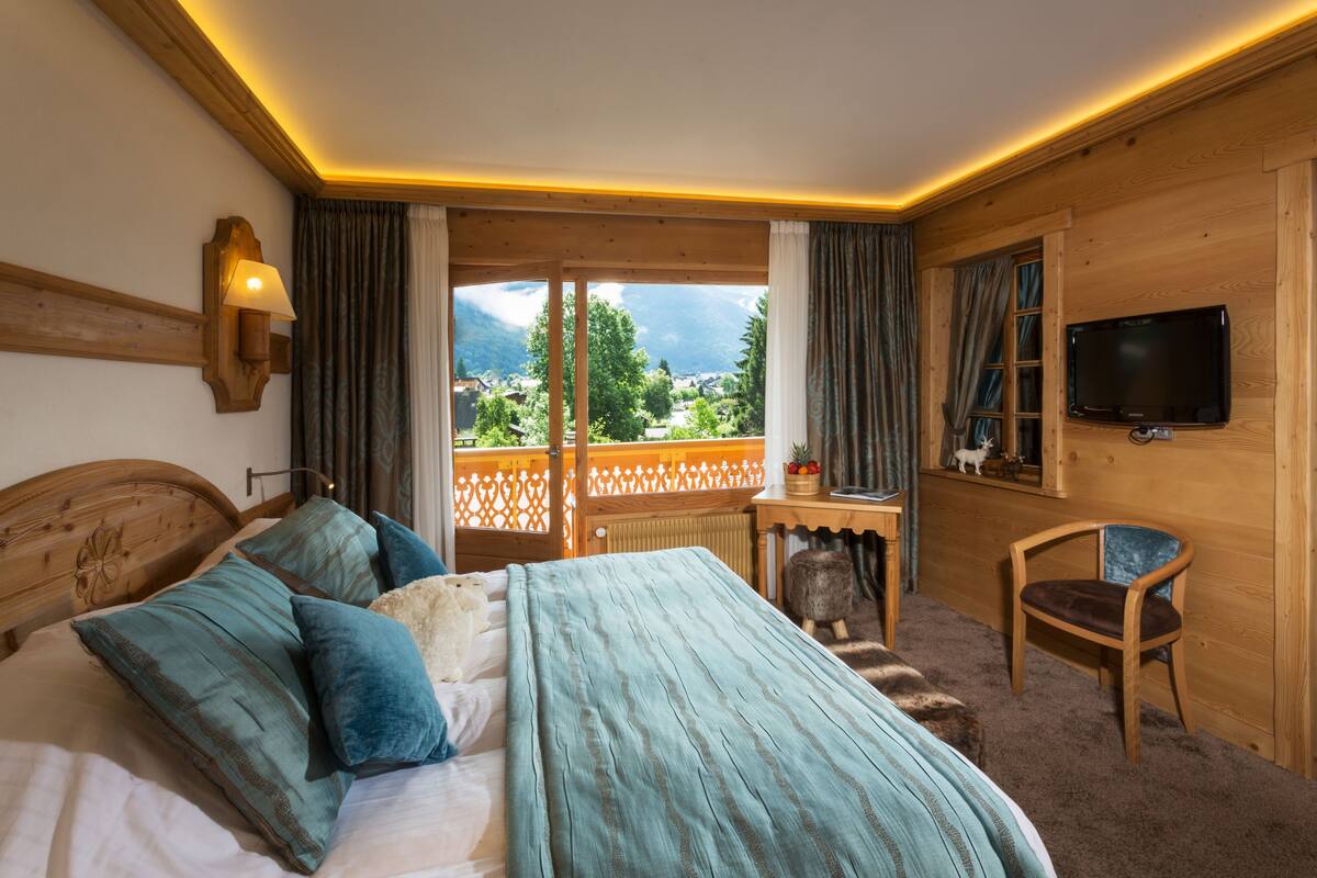 A bedroom with a bed, a chair, a TV, and a view of the outdoors.