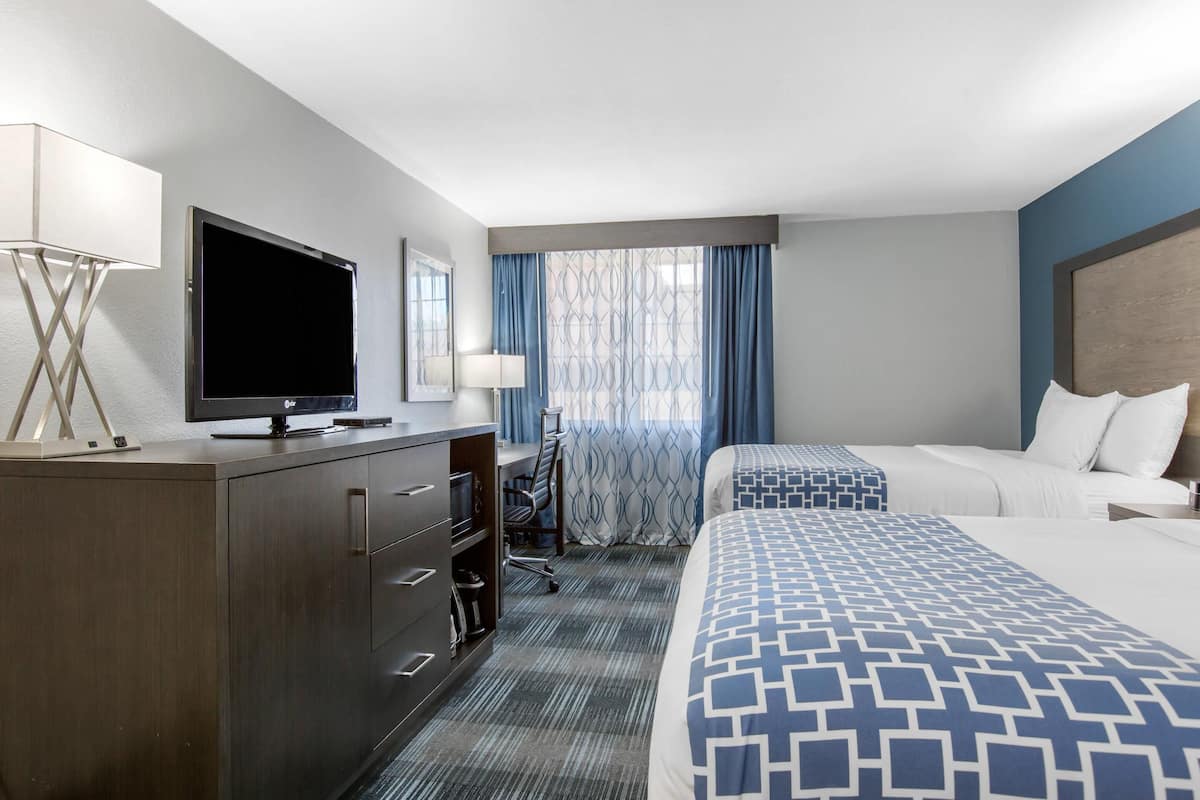 Une chambre d’hôtel avec un lit, un bureau avec un ordinateur, une télévision et une fenêtre avec des rideaux.