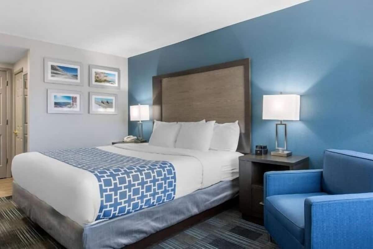 Une chambre d’hôtel avec un lit, deux lampes de chevet, un fauteuil bleu et des tableaux encadrés au mur.