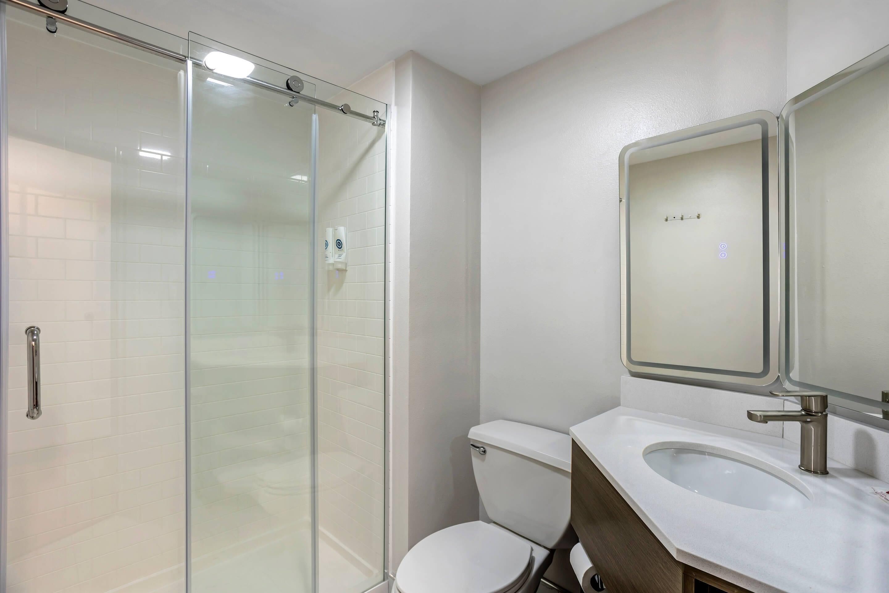 Un baño con cabina de ducha de vidrio, inodoro y lavabo con espejo.