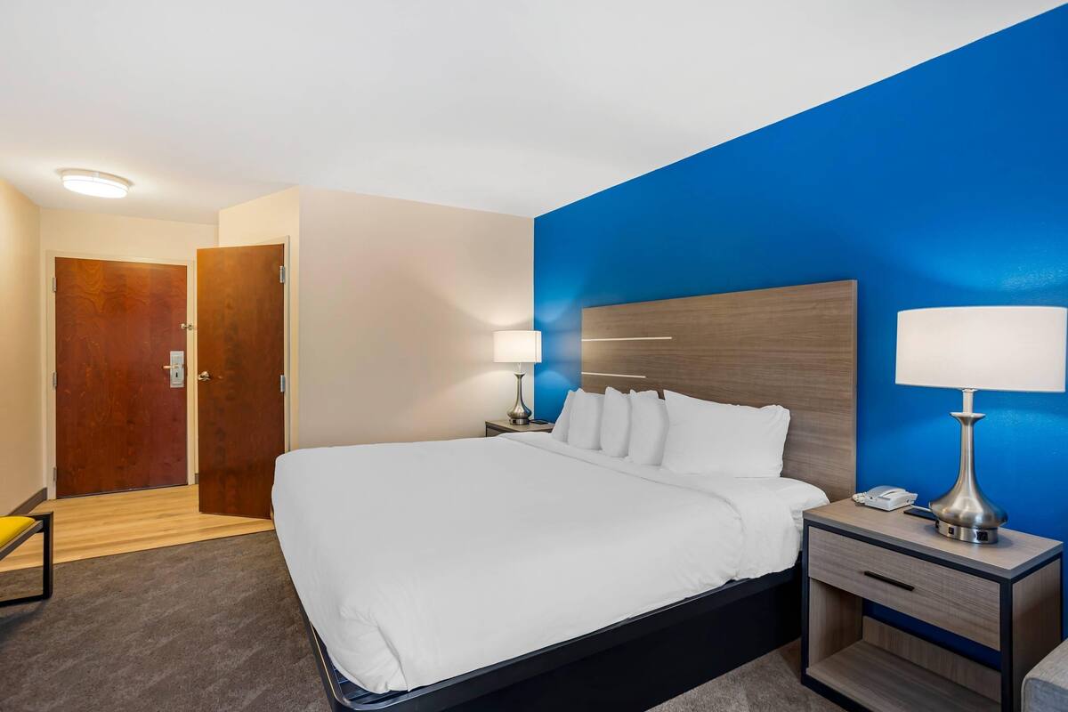 A hotel room with a large bed, bedside lamps, a wooden headboard, and a desk with a phone.
