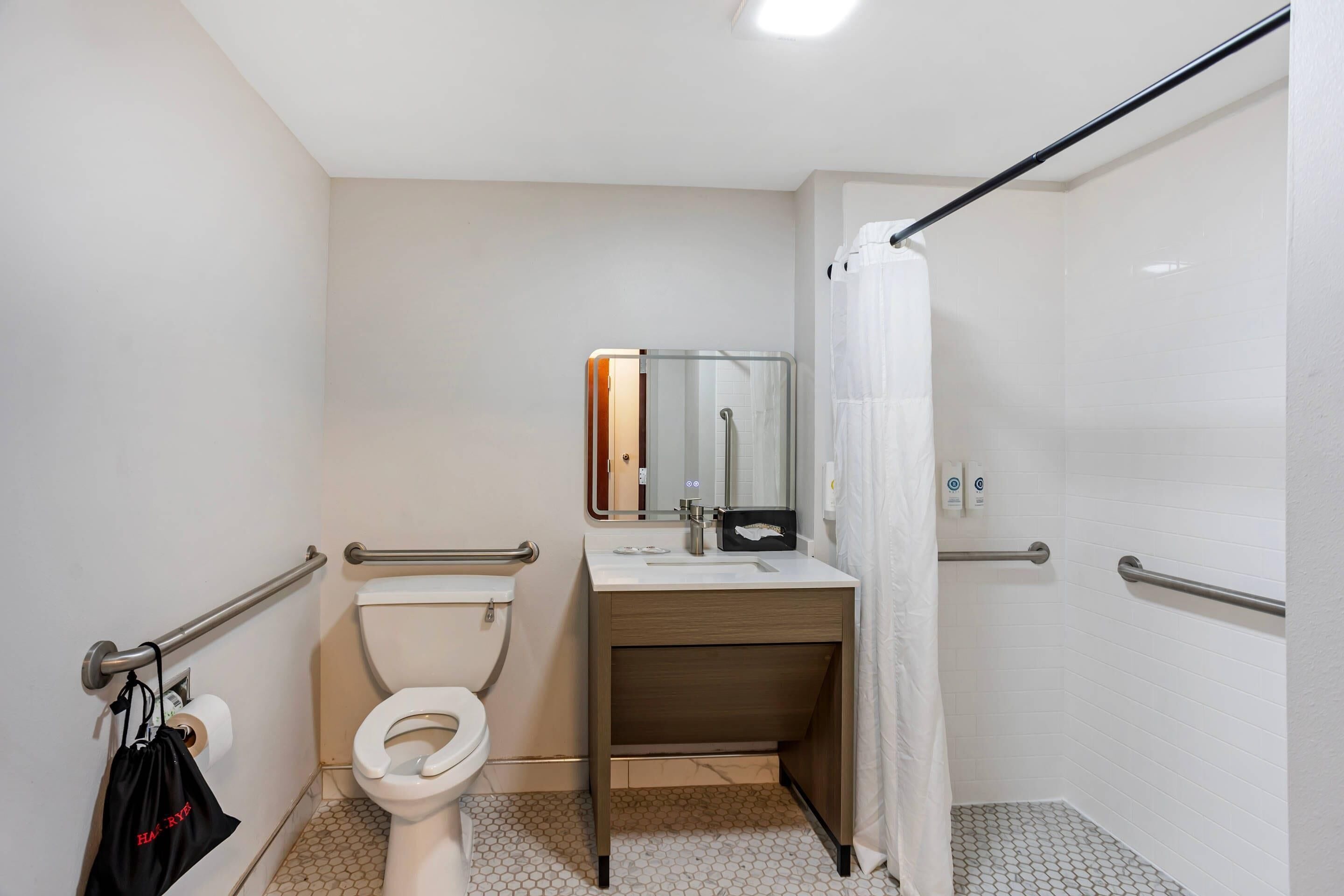 A bathroom with a toilet, sink, mirror, and shower area.