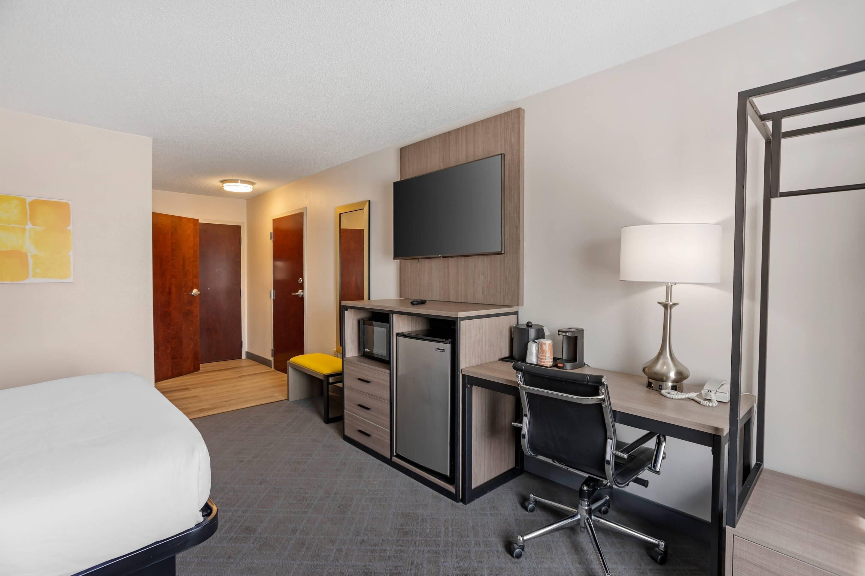 A hotel room with a bed, desk, chair, TV, and a small refrigerator.
