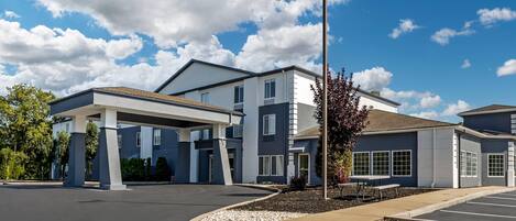 A modern building with a covered parking area, a clear sky, and a well-maintained landscape.