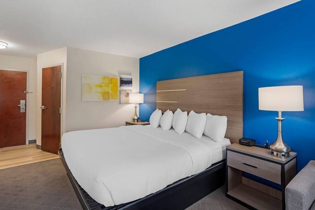 A hotel room with a large bed, two bedside tables with lamps, a wooden headboard, and a blue accent wall.