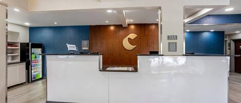 A reception desk with a wooden wall and a crescent logo, a refrigerator with drinks, and a blue wall.