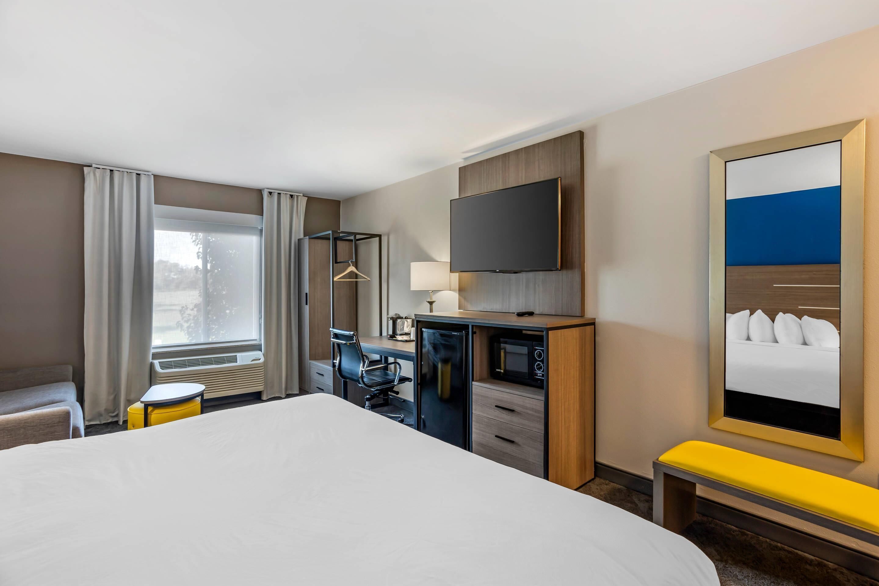 A hotel room with a large bed, a desk with a chair, a television, a mirror, and a window with curtains.