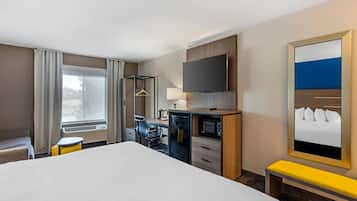 Una camera d'albergo con un letto grande, una scrivania con una sedia, una televisione, uno specchio e una finestra con tende.