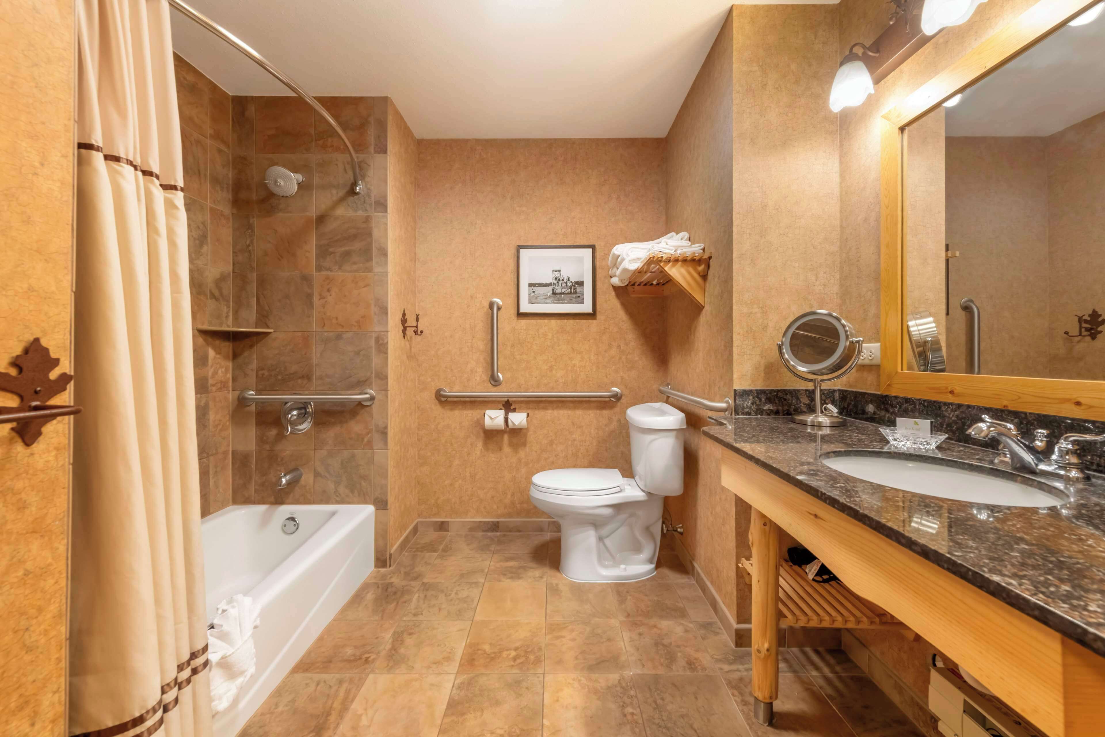 A bathroom with a bathtub, toilet, and sink, equipped with a shower, grab bars, and a mirror.