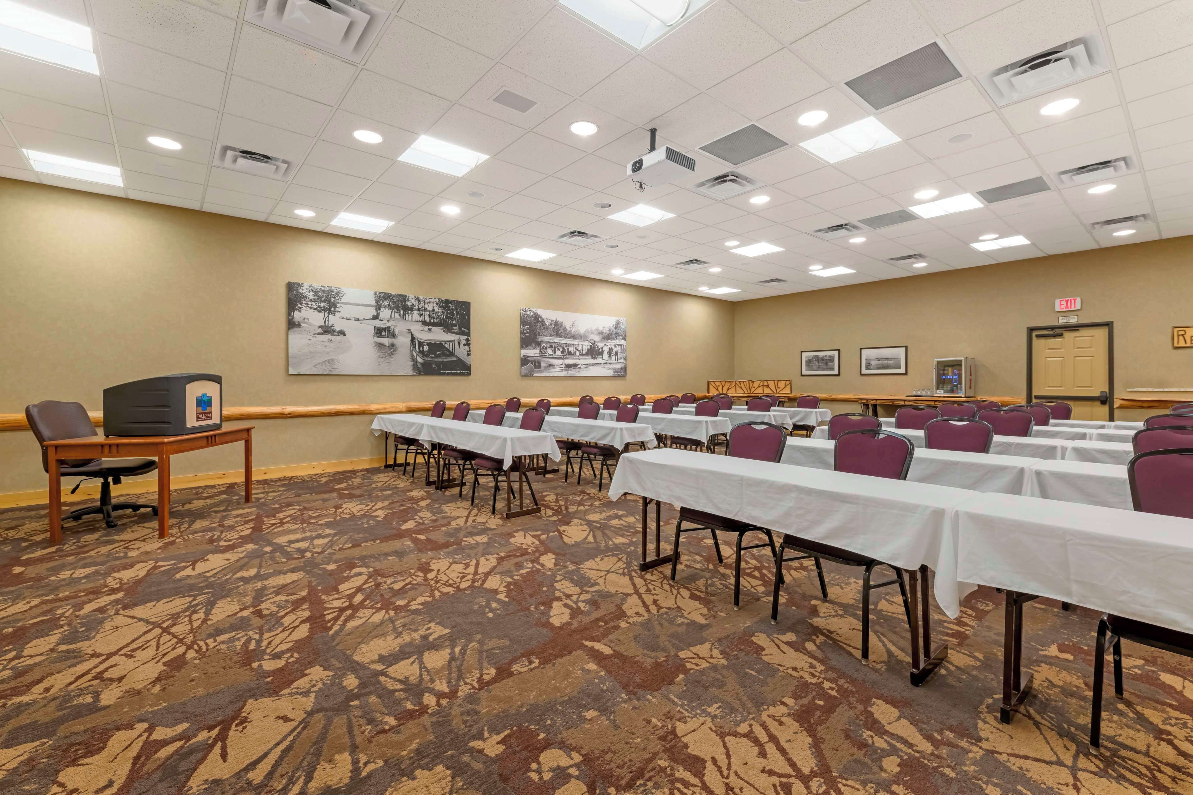 Un salón de conferencias con mesas, sillas y una pantalla de proyector.