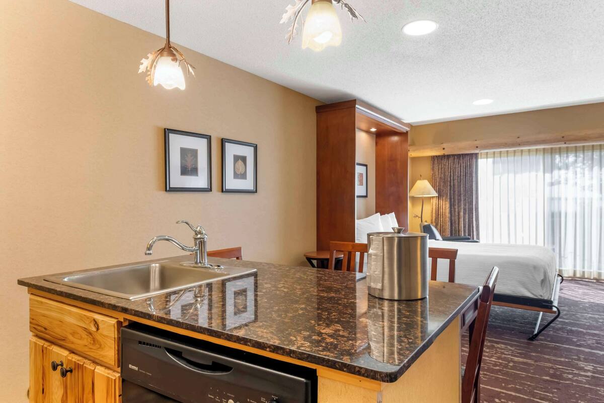A hotel room with a kitchen area, a bed, and a window with curtains.