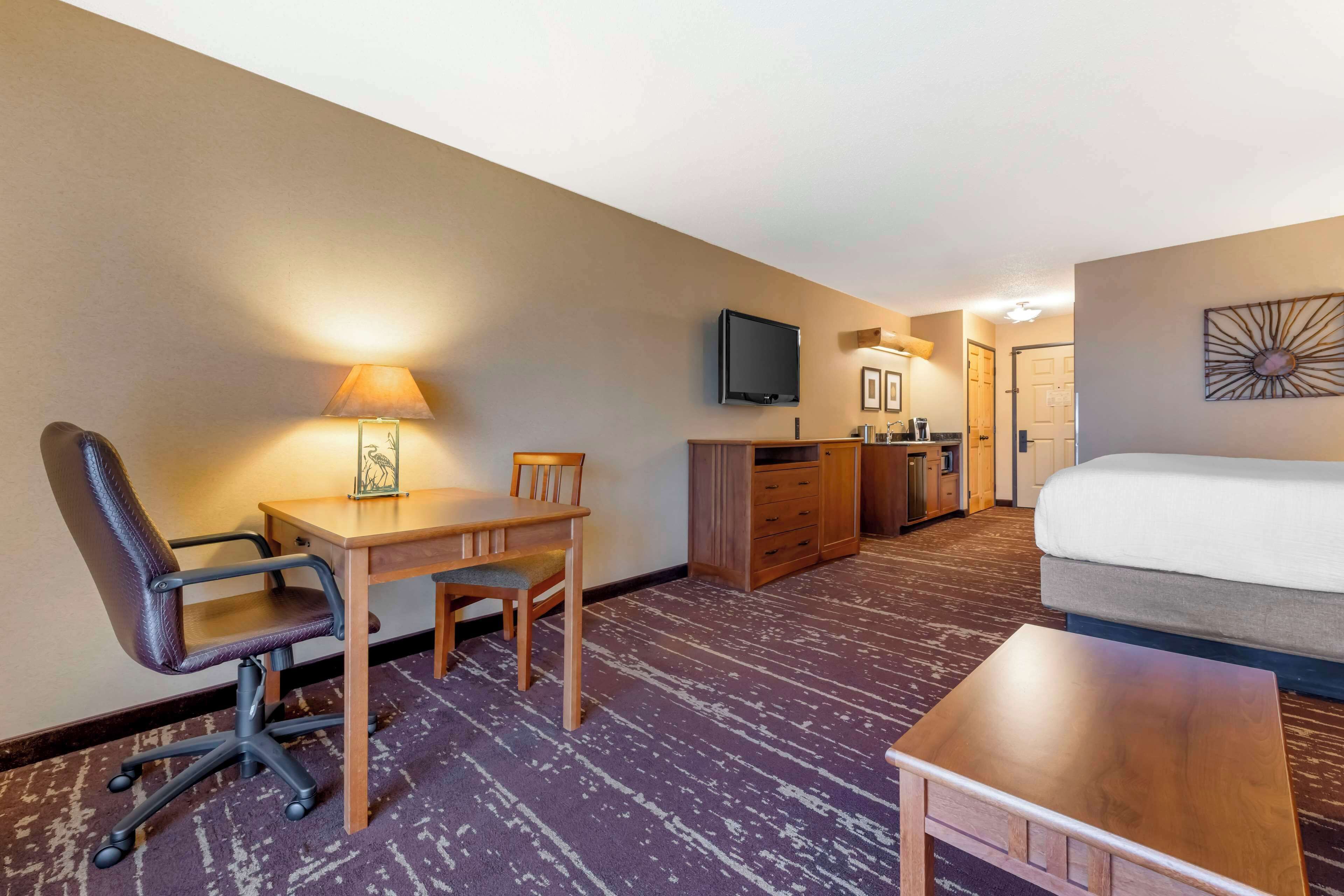 A hotel room with a bed, a desk with a chair, a television, and a small table.
