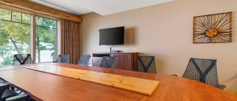 Een vergaderruimte met een lange houten tafel, diverse stoelen, een flatscreen televisie aan de muur en een decoratief wandobject.