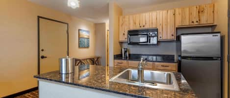 A modern kitchen with granite countertops, stainless steel appliances, wooden cabinets, and pendant lighting.