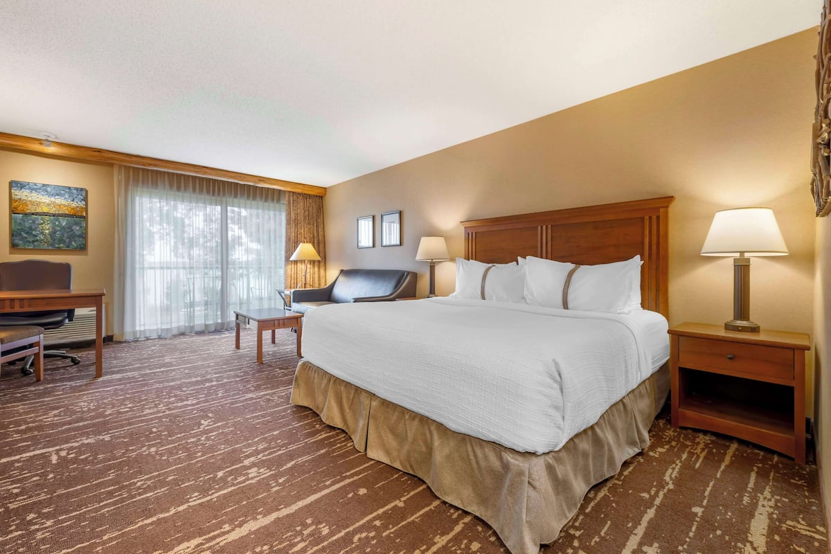 A hotel room with a large bed, a desk, two chairs, a lamp, and a painting on the wall.