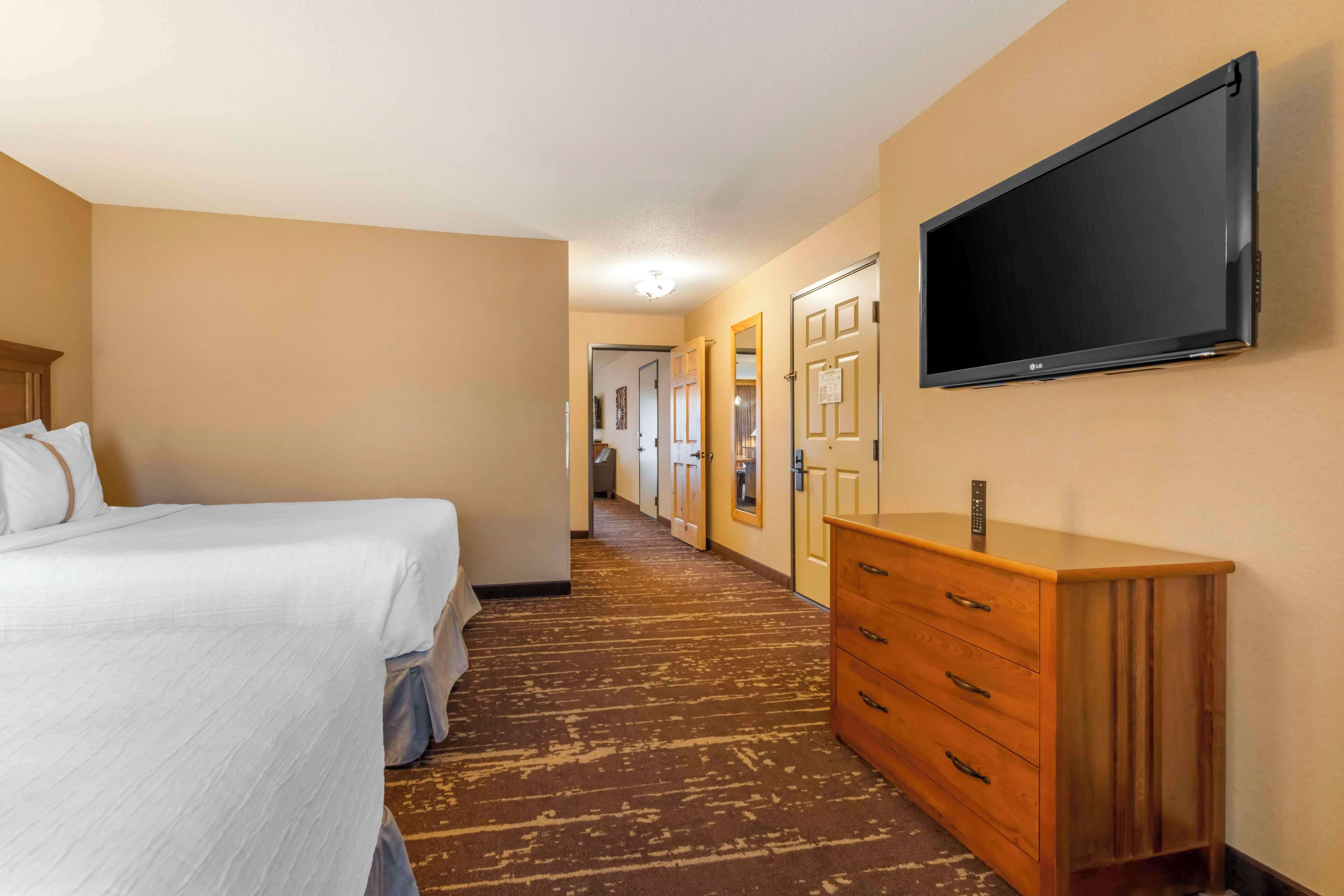 Une chambre d’hôtel avec un lit, une commode en bois et un téléviseur fixé au mur.