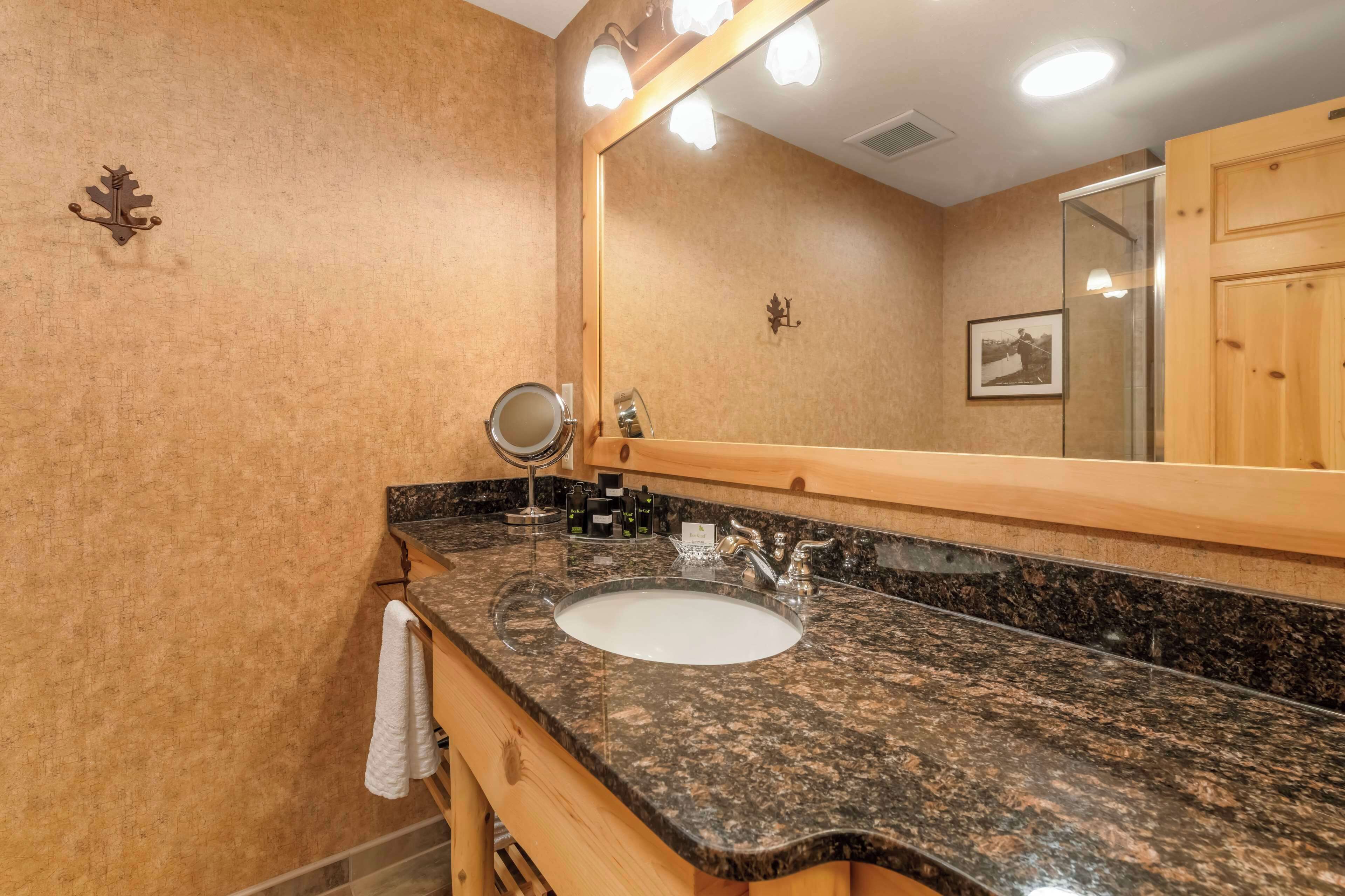 Un baño con lavamanos de encimera de granito, espejo y tocador de madera.