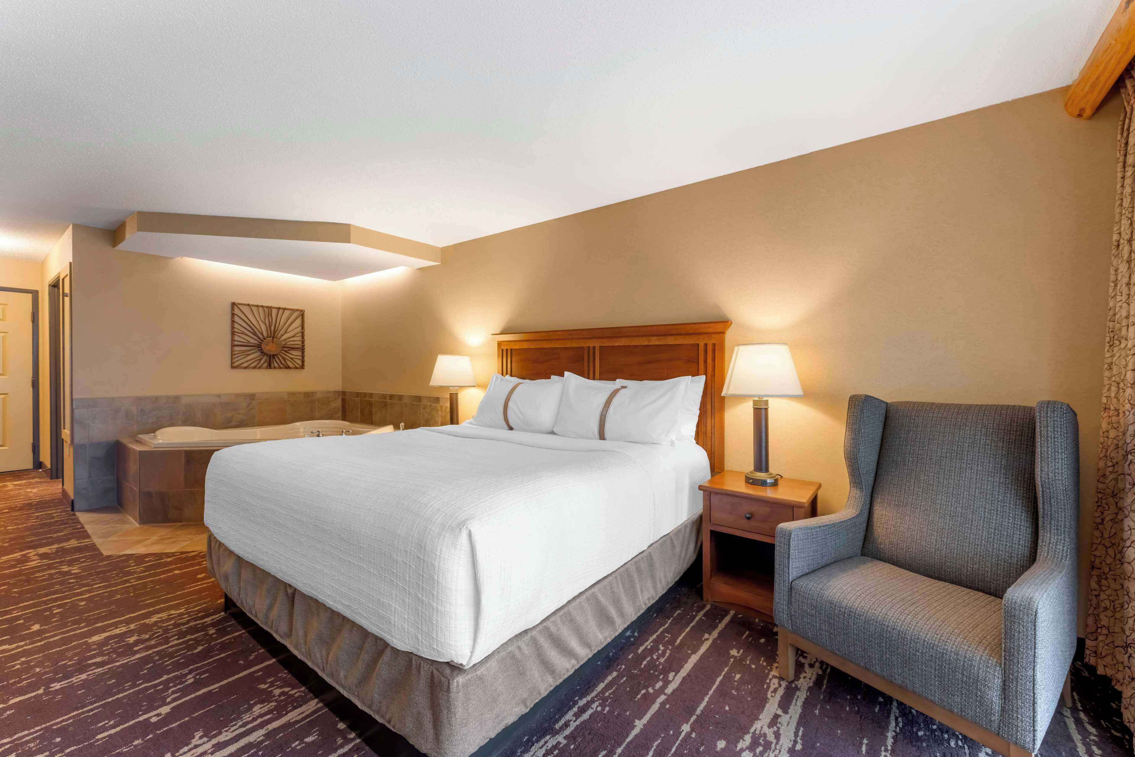 Habitación de hotel con una cama grande, una silla, una mesita de noche y una obra de arte colgada en la pared.