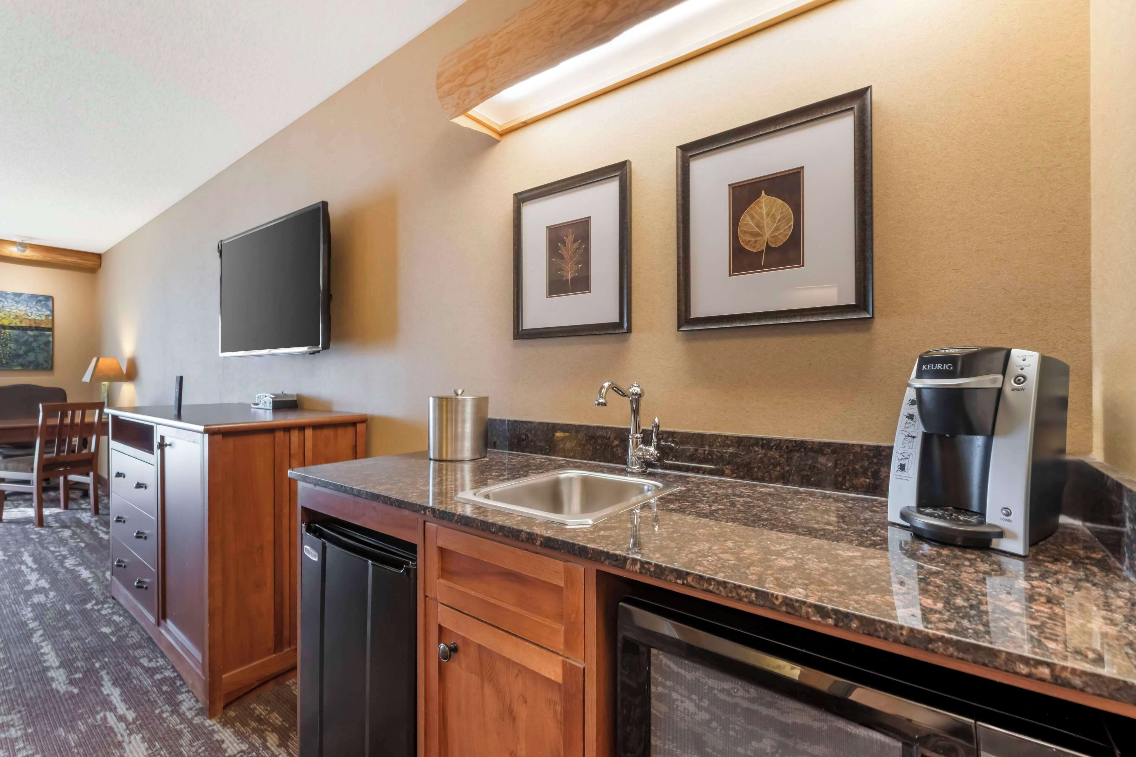 A hotel kitchen with a granite countertop, stainless steel sink, and a Keurig coffee maker.
