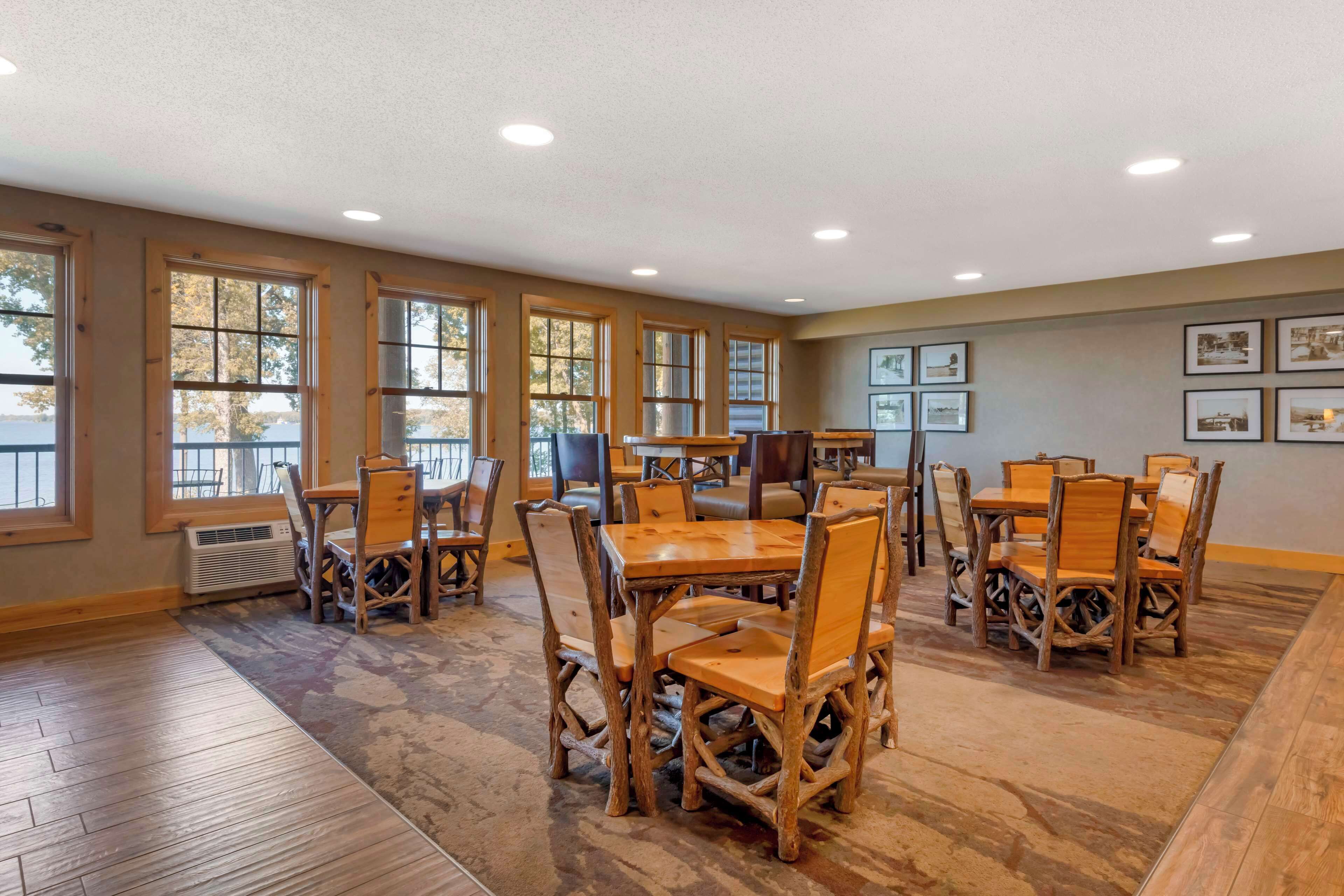 A spacious room with large windows, wooden tables and chairs, and framed pictures on the walls.
