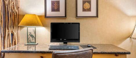A wooden desk with a computer monitor, keyboard, and mouse. There are two framed pictures on the wall above the desk.