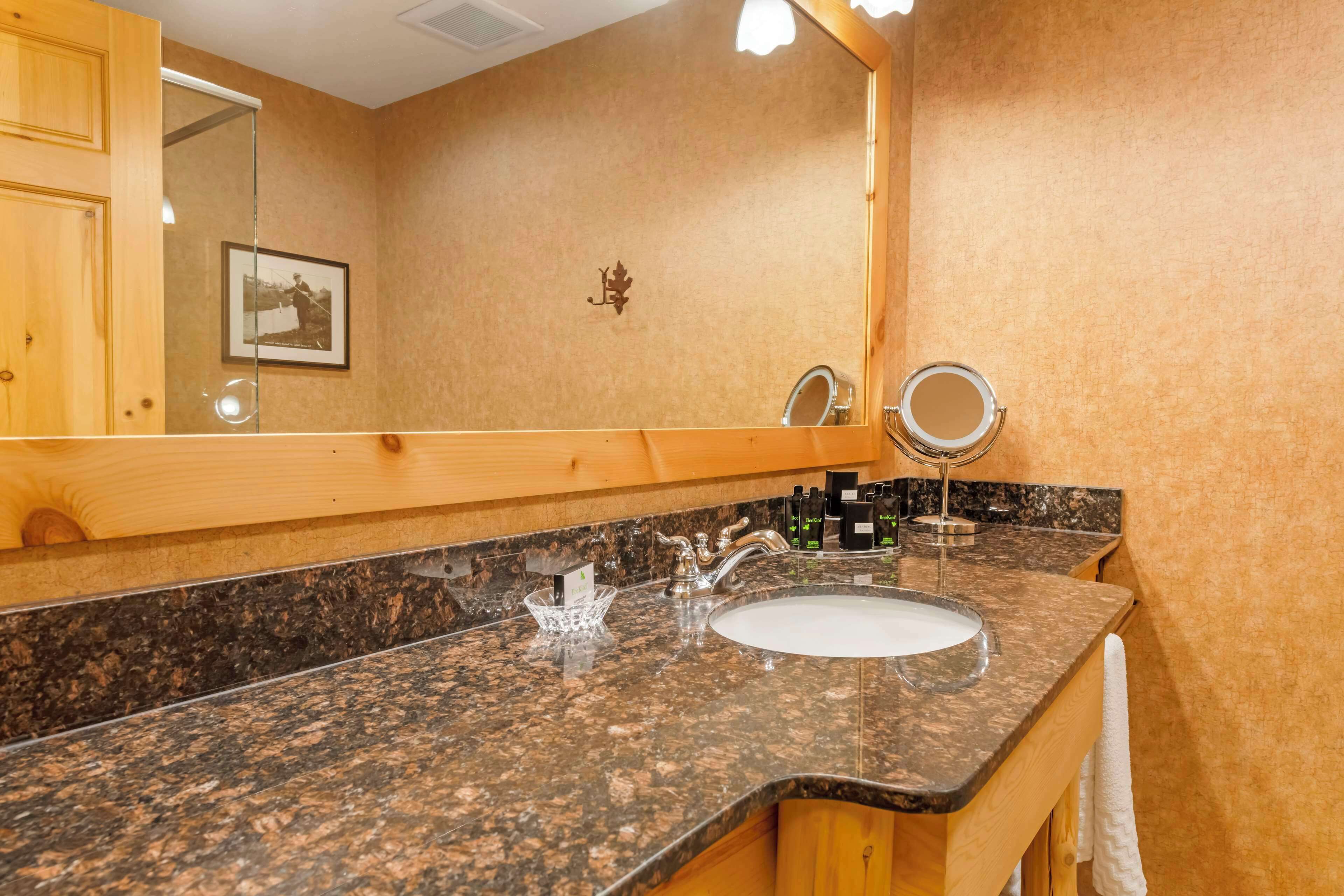 A bathroom with a granite countertop, a sink, a mirror, and wooden cabinets.