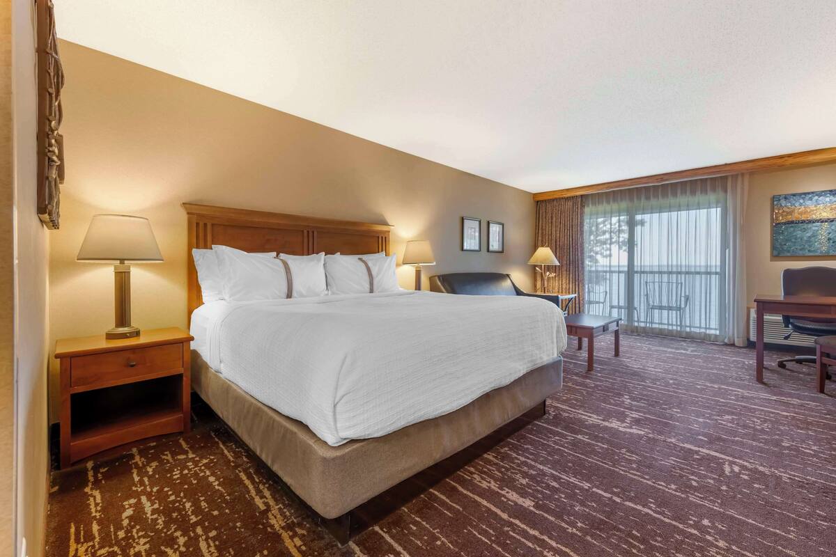 A hotel room with a large bed, two bedside tables with lamps, a desk, and a chair.