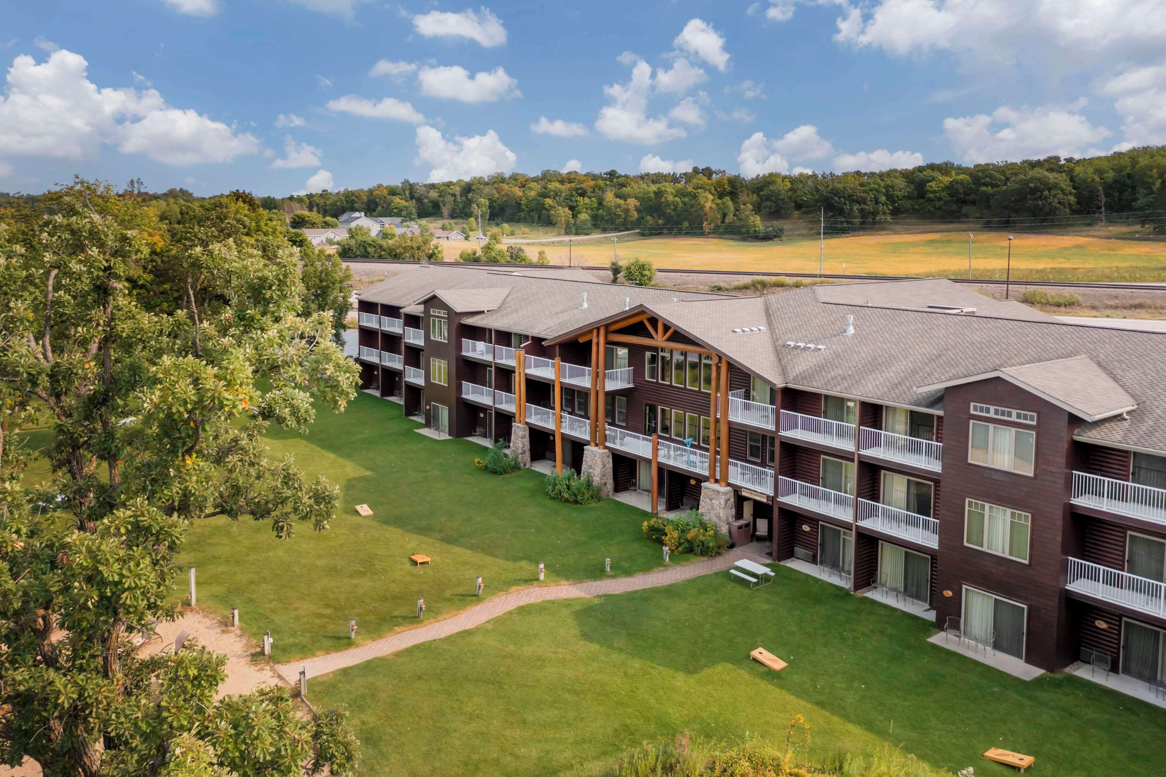 A multi-story hotel with balconies, a well-maintained lawn, and a view of a sports field.