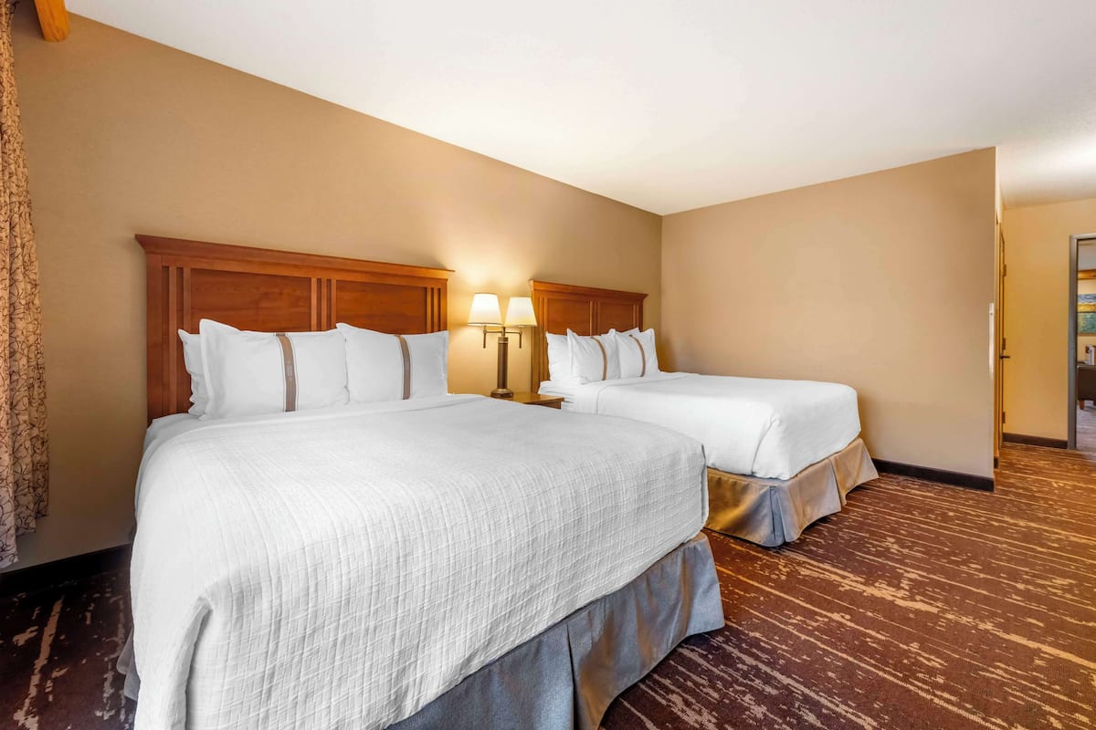A hotel room with two beds, a wooden headboard, a nightstand with lamps, and a patterned carpet.