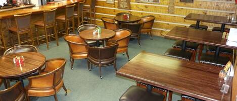Un interno ristorante con tavoli e sedie in legno, un'area bar e una parete con targhe storiche.