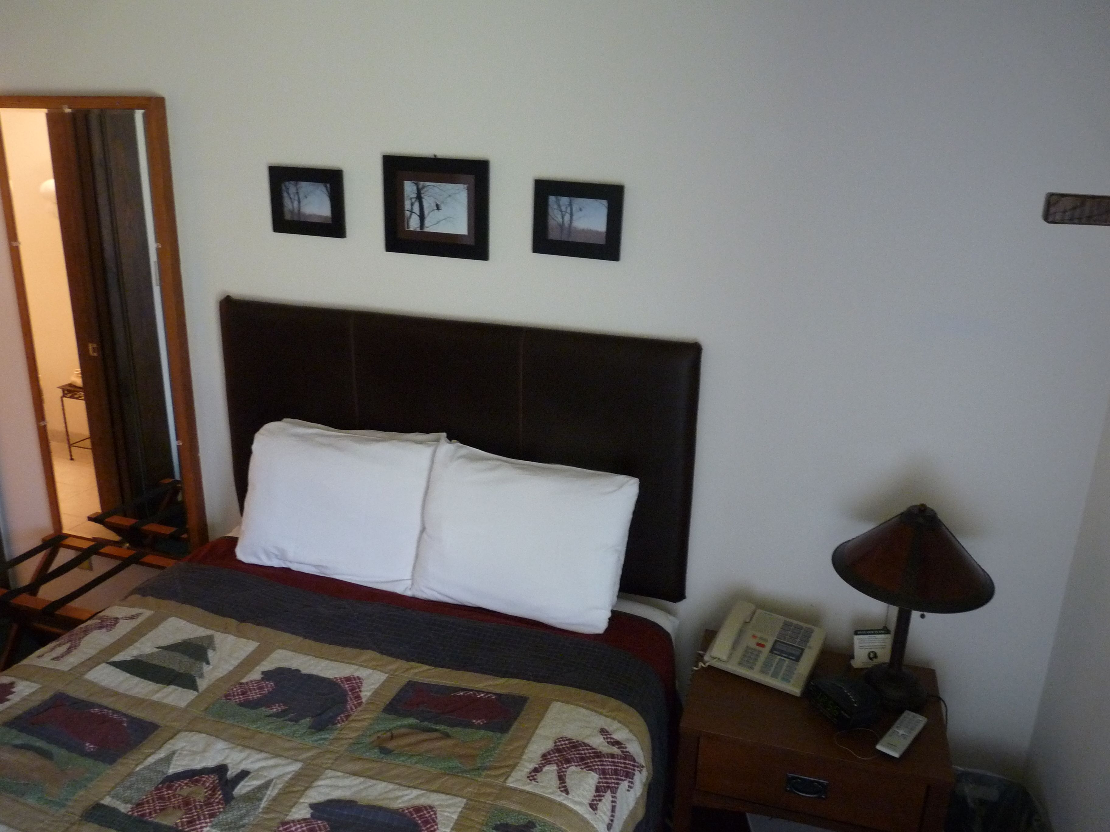 Una camera d'albergo con un letto, un comodino con una lampada e tre quadri appesi al muro.