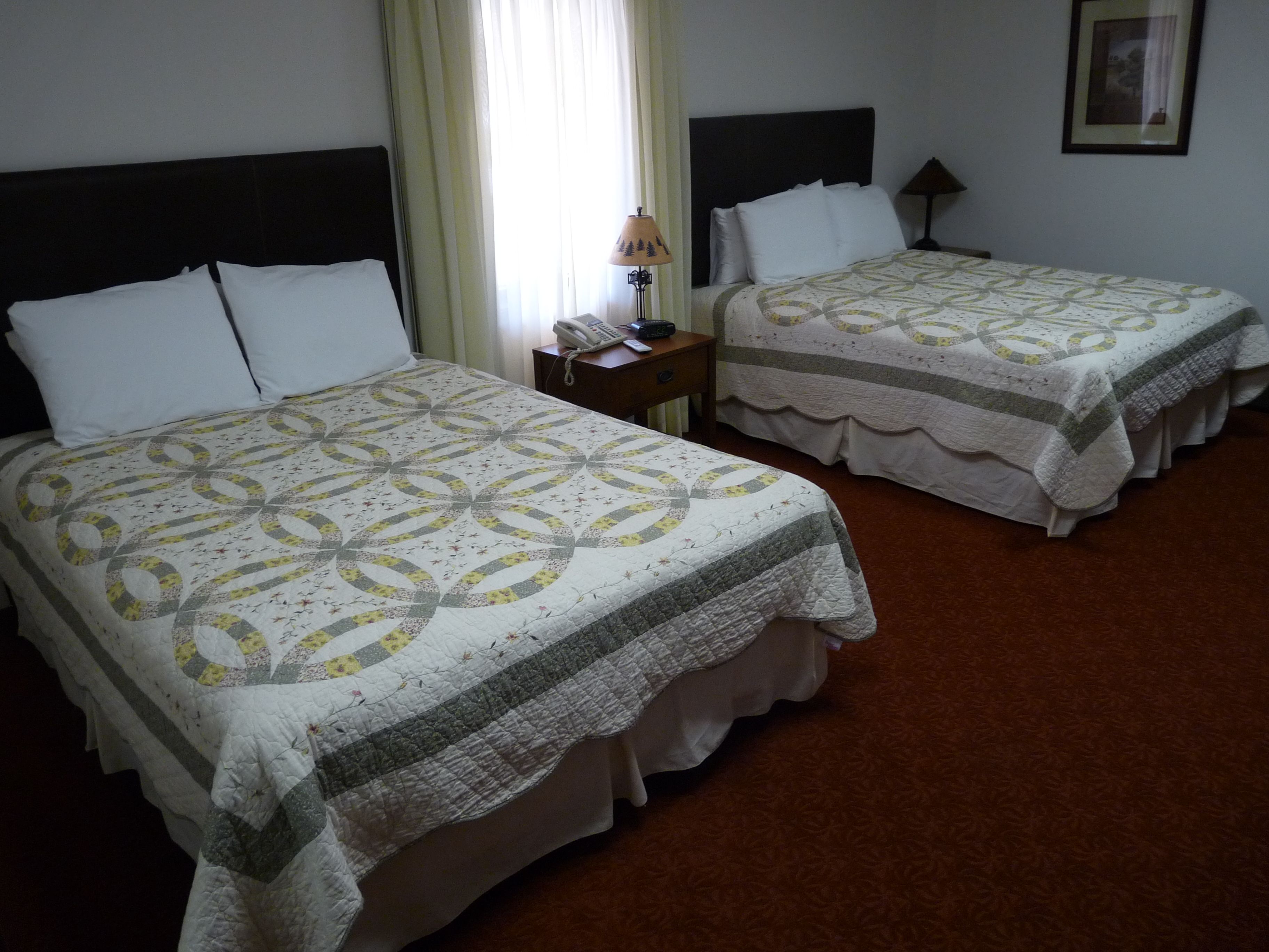 Two beds with patterned quilts, a bedside table with a lamp, and a framed picture on the wall.