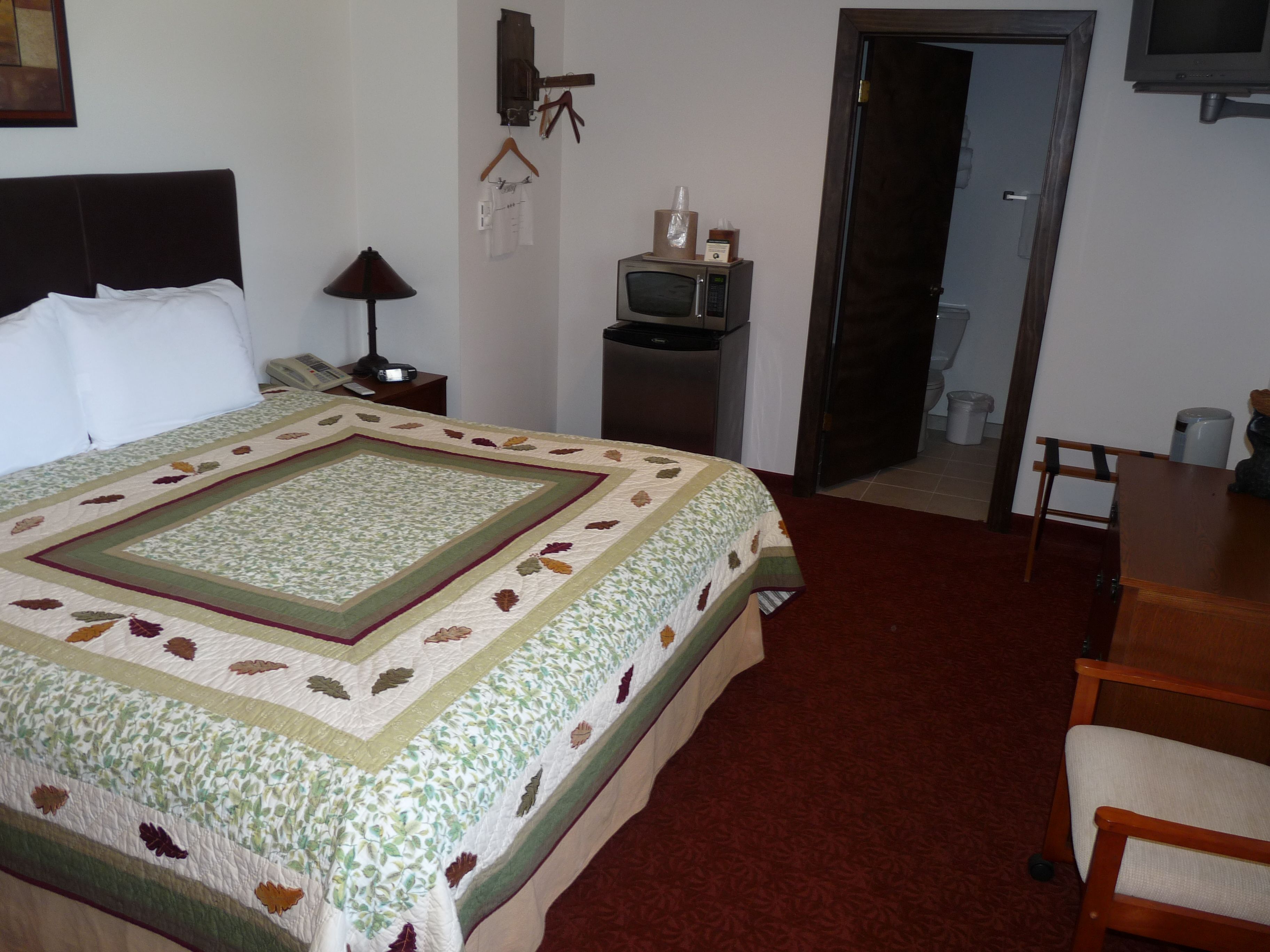 A hotel room with a large bed, a desk, a television, and a bathroom visible through an open door.