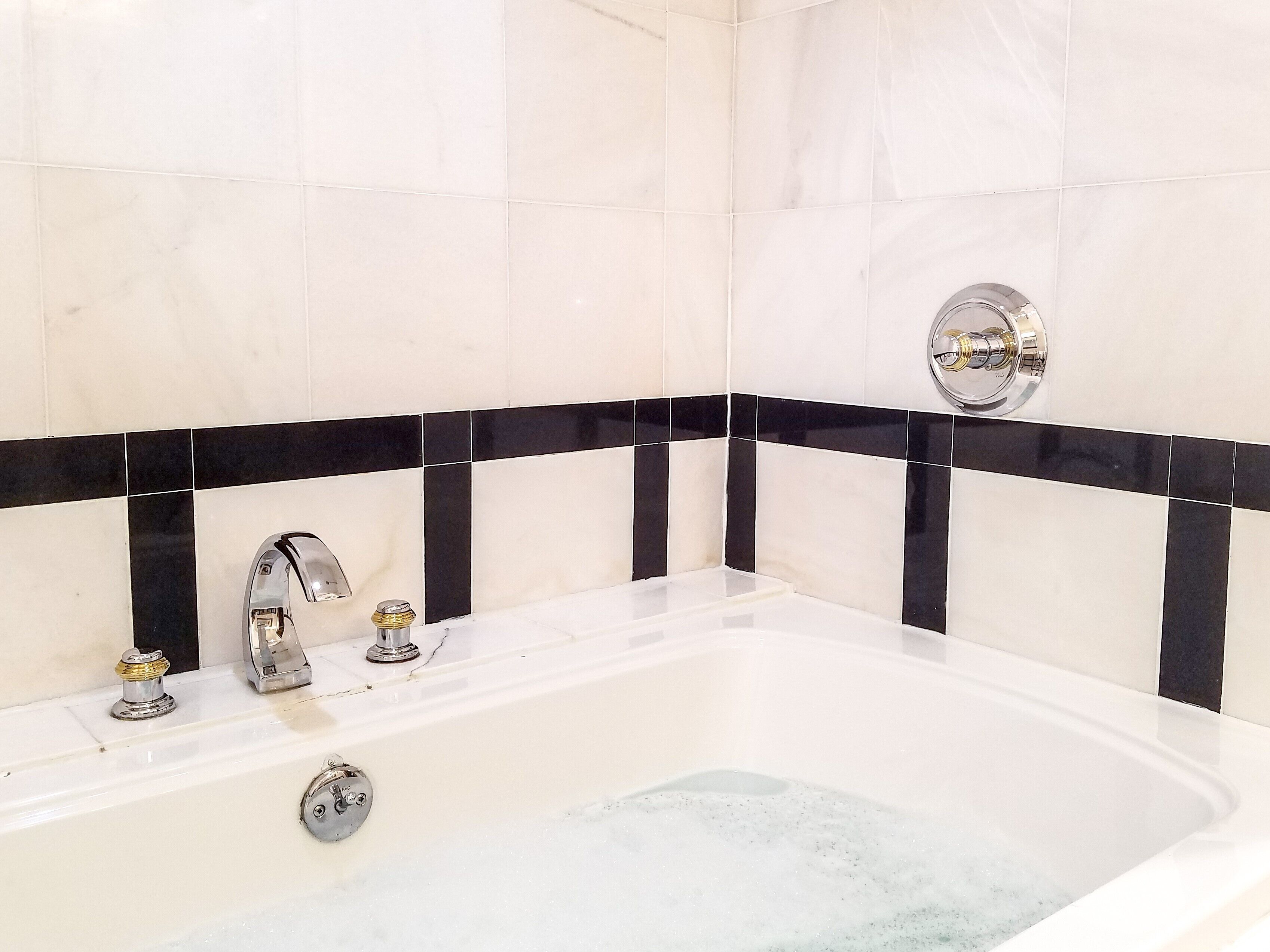 A bathroom with a white bathtub, black and white tiled walls, and a chrome faucet.