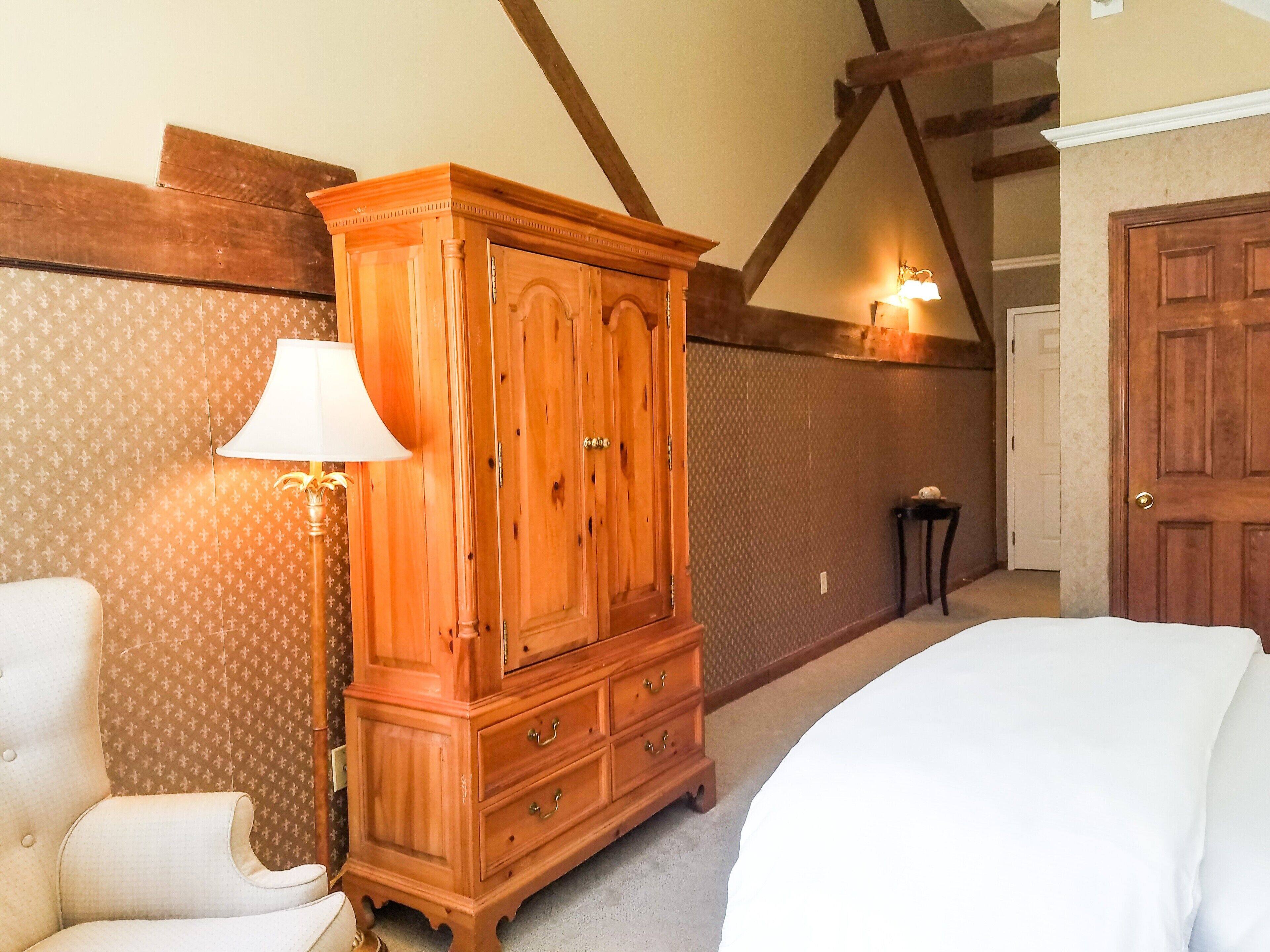 A bedroom with a wooden wardrobe, a bedside lamp, a patterned wallpaper, and a door.