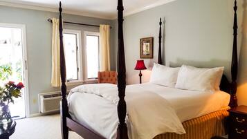 A four-poster bed with white linens, a red lamp, and a framed picture on the wall.