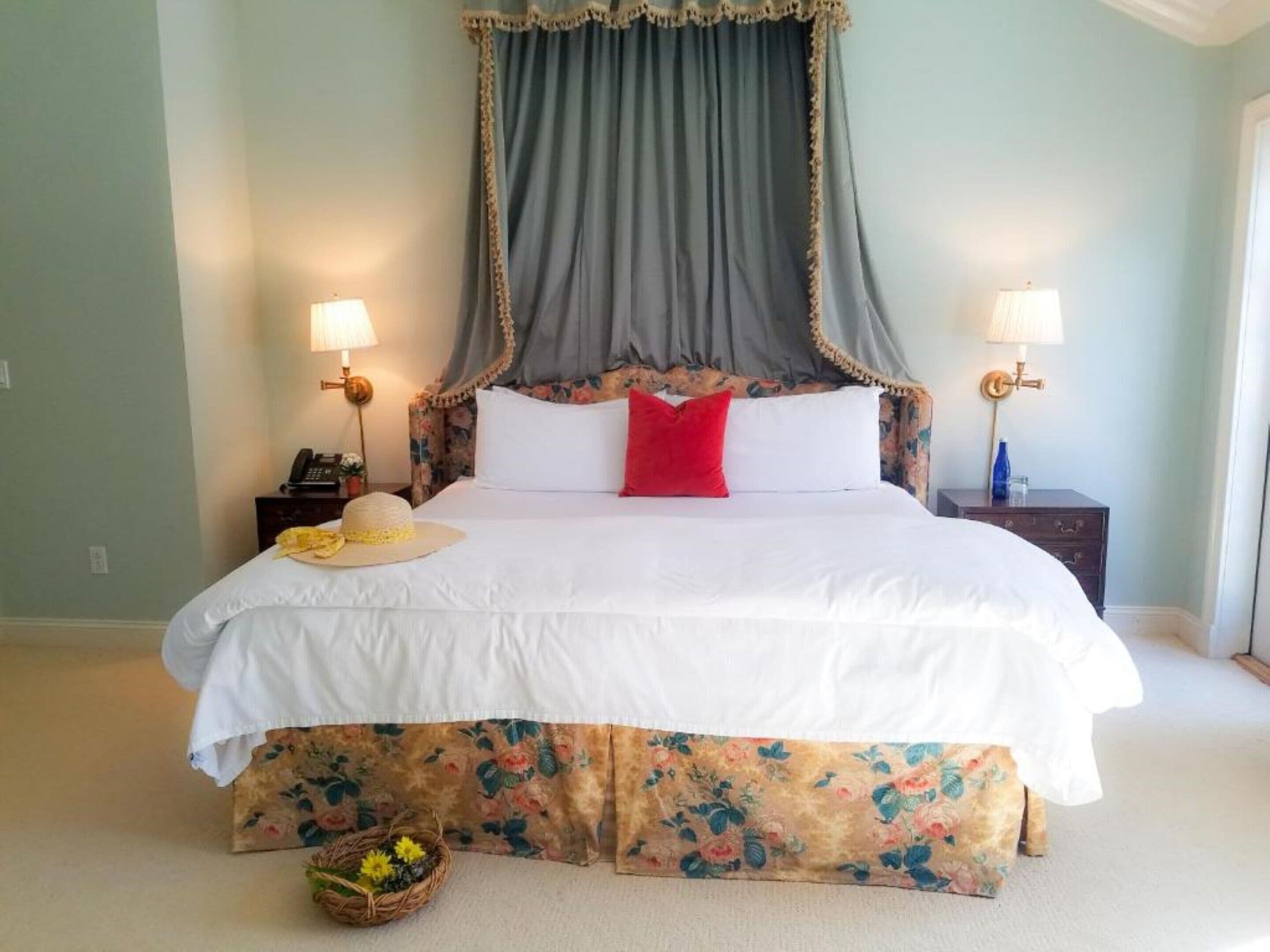 A bed with a canopy, two bedside tables with lamps, a telephone, and a basket with flowers.