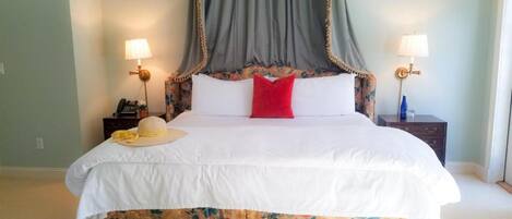 A bed with a canopy, two bedside tables with lamps, a telephone, and a basket with flowers.