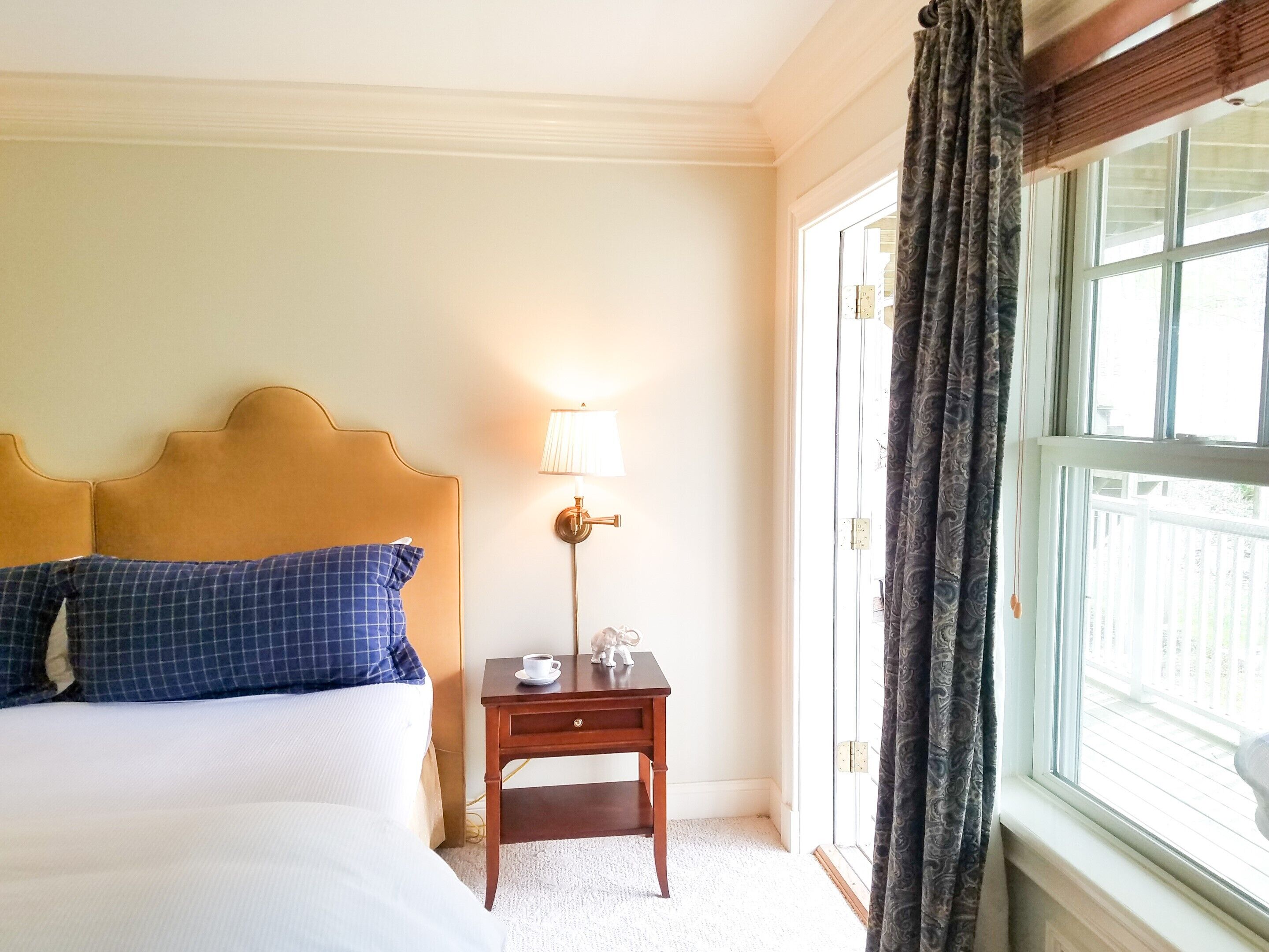 A hotel room with a bed, a nightstand with a lamp, and a window with curtains.